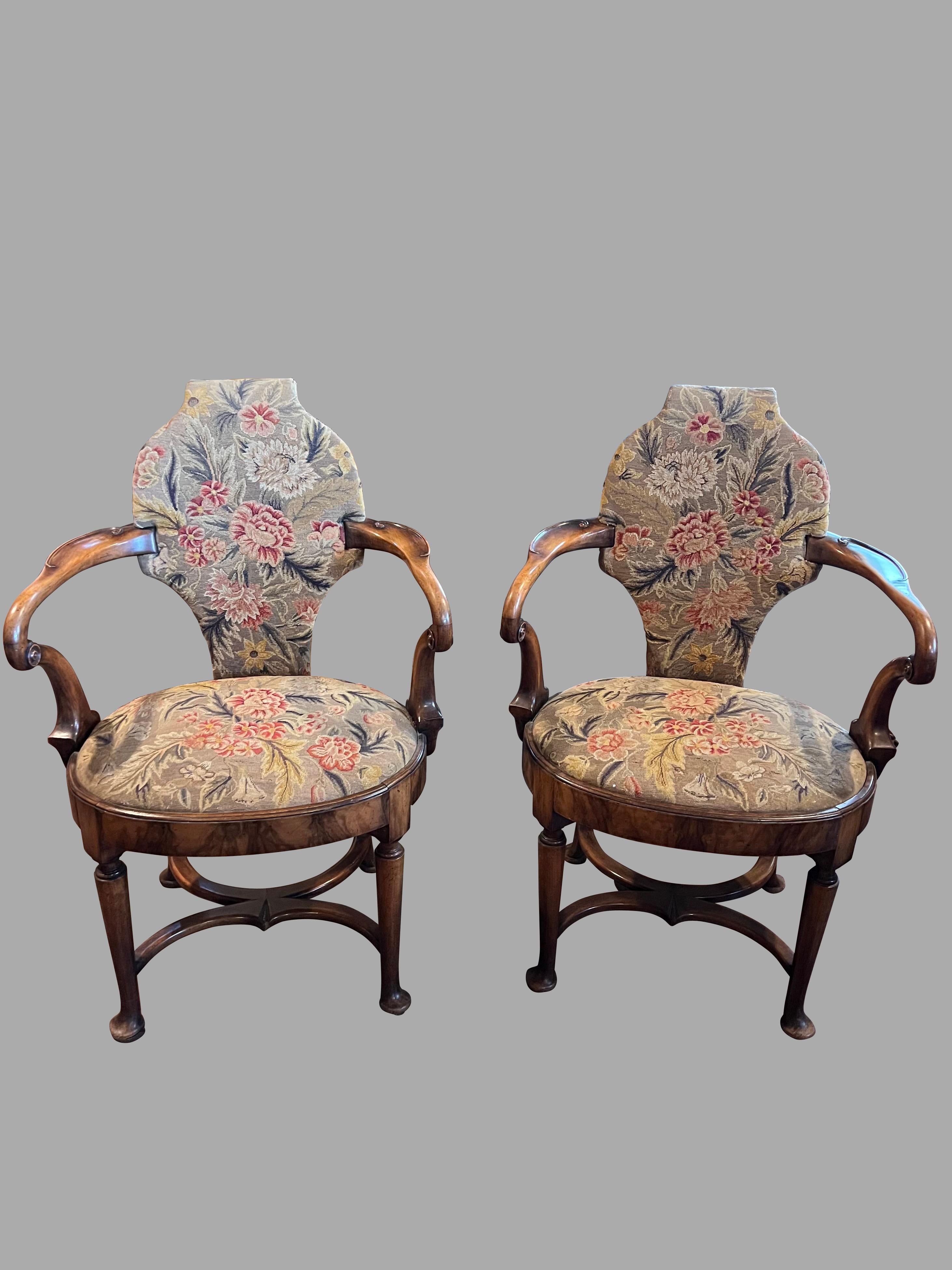 Un'insolita coppia di poltrone aperte in stile George II rivestite in noce, con schienale sagomato e braccioli a croce di pastore che terminano in un'apertura ovale.  sede. Le sedie sono sostenute da gambe tornite che terminano con piedi a pad.