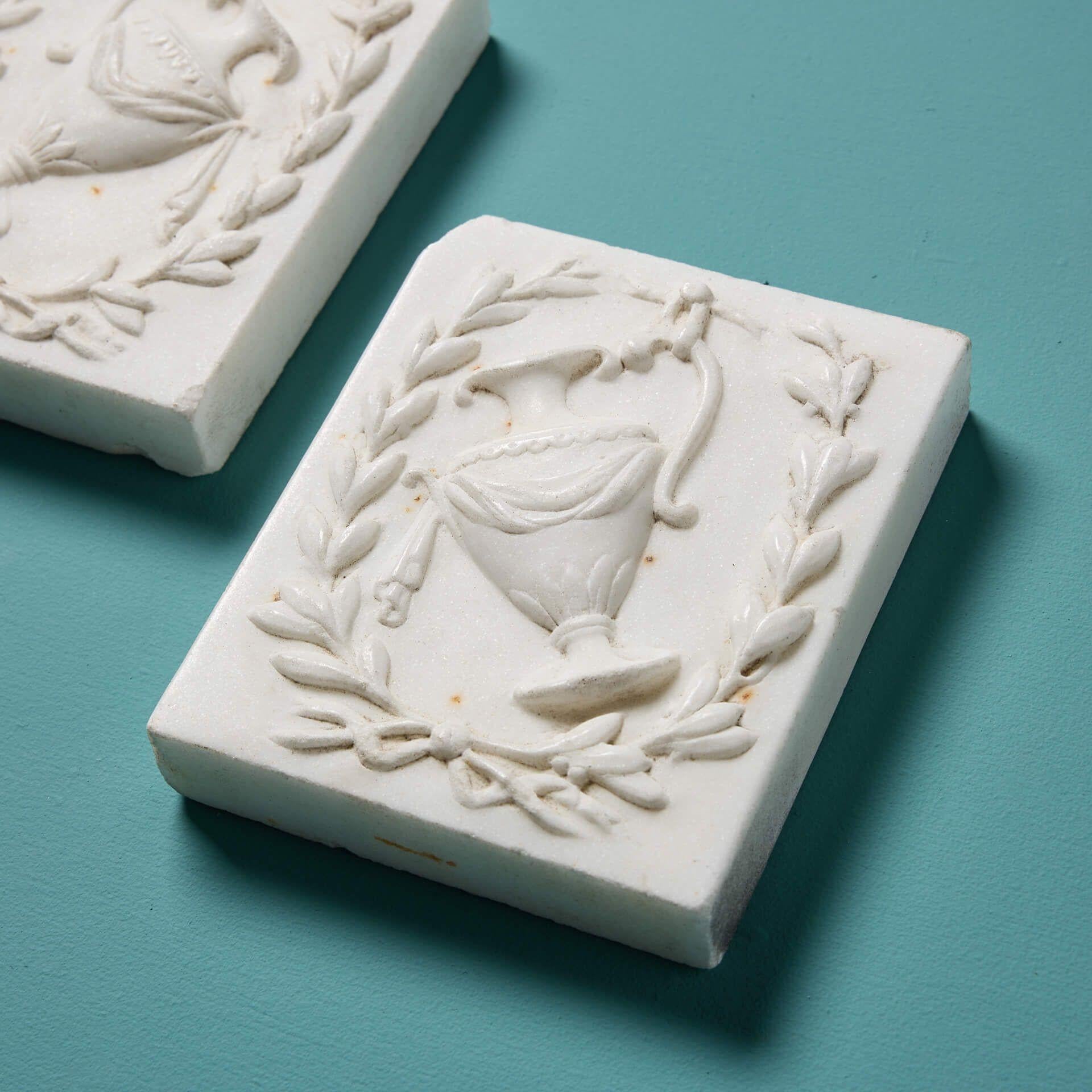 A beautiful pair of late Georgian era white statuary marble plaques carved with neoclassical pitchers and laurel wreaths, originally used as corner blocks for an English Georgian fireplace.

Dating to circa 1800, these plaques are over 220 years old