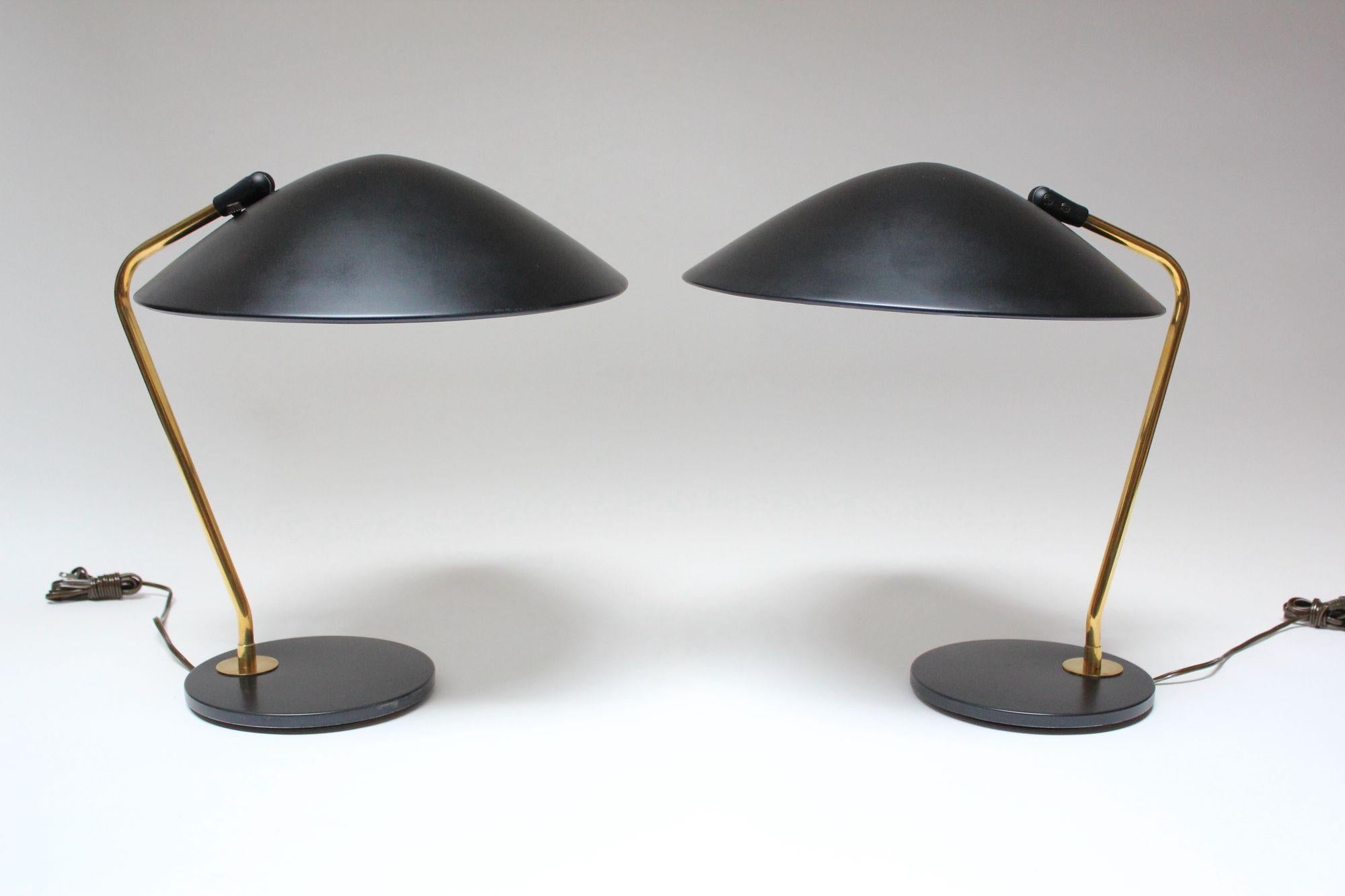 Pair of tables lamps designed by Gerald Thurston for Lightolier composed of oversized, fully-adjustable, black-metal shades and corresponding round bases with brass stems (ca. 1950s, USA).
Black paint has been conservatively touched up and brass is