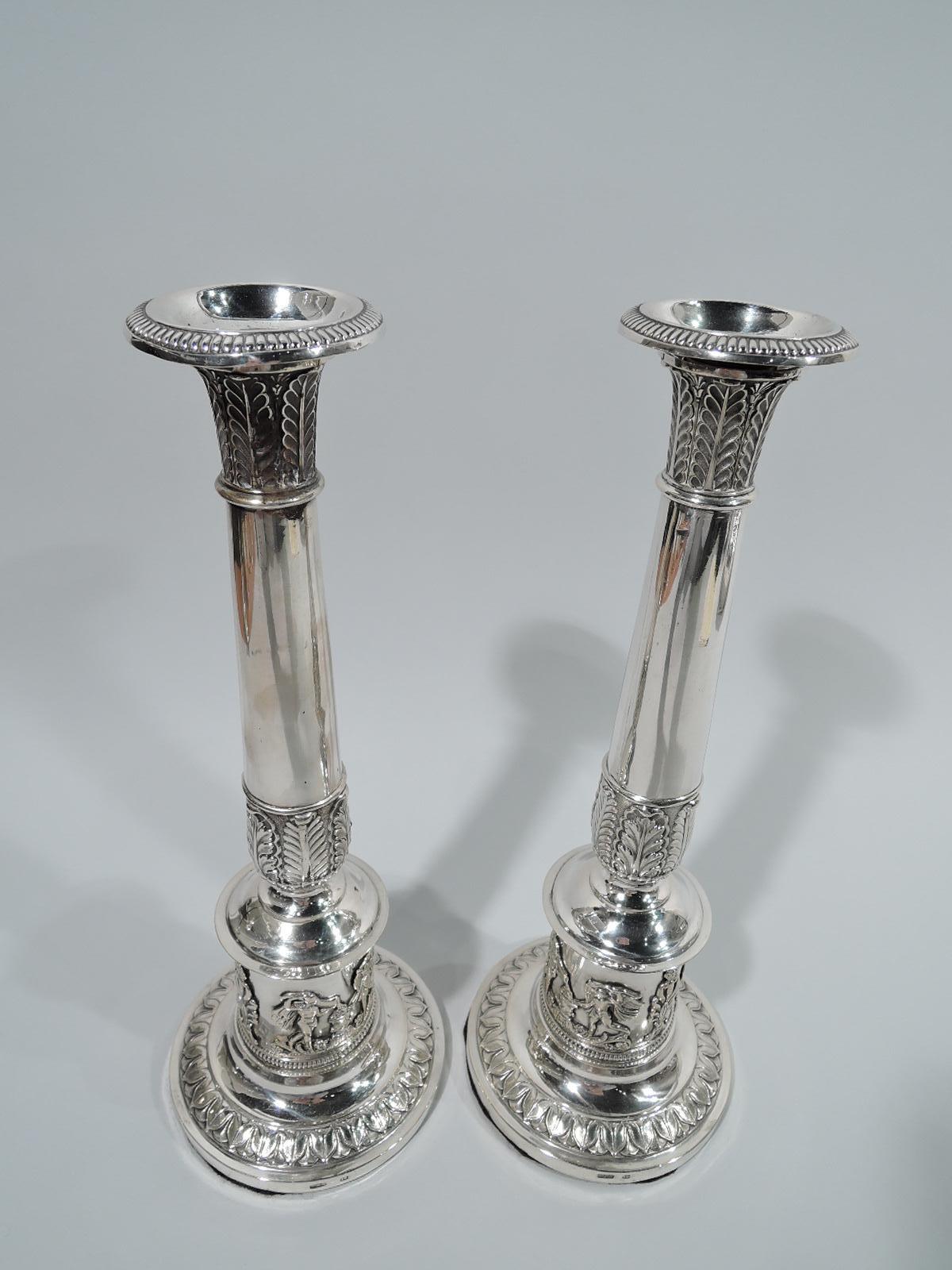 Pair of German Biedermeier classical silver candlesticks, circa 1820. Each: Upward tapering shaft on columnar base on raised foot. Classical ornamental borders with gadrooning, leaf-and-dart, and leaf. On base is applied frieze depicting golden