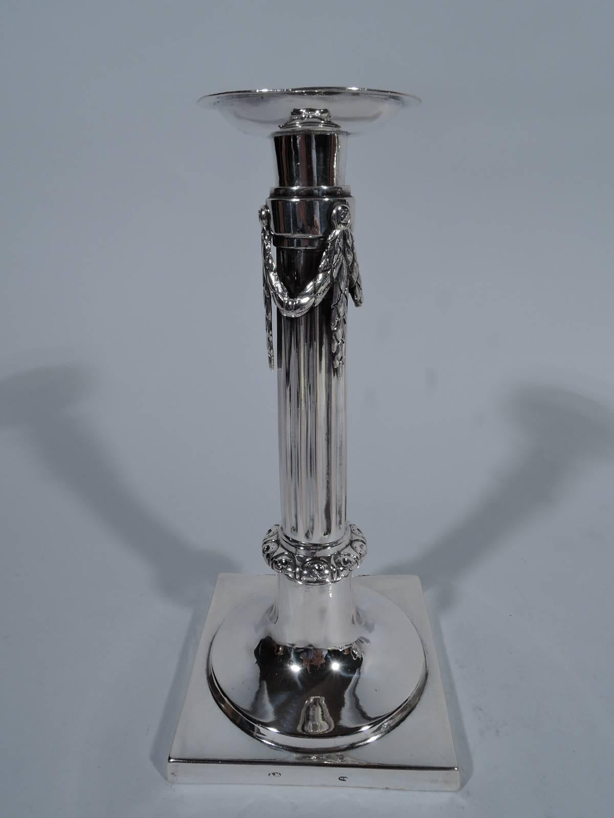 Pair of German Biedermeier silver candlesticks, circa 1840. Each: Fluted column mounted to square base. Leaf garland mounted to top. Tooled leaf-and-dart knop at column base. Detachable bobeches. Spare classicism. Hallmarked. Total weight: 16.2 troy