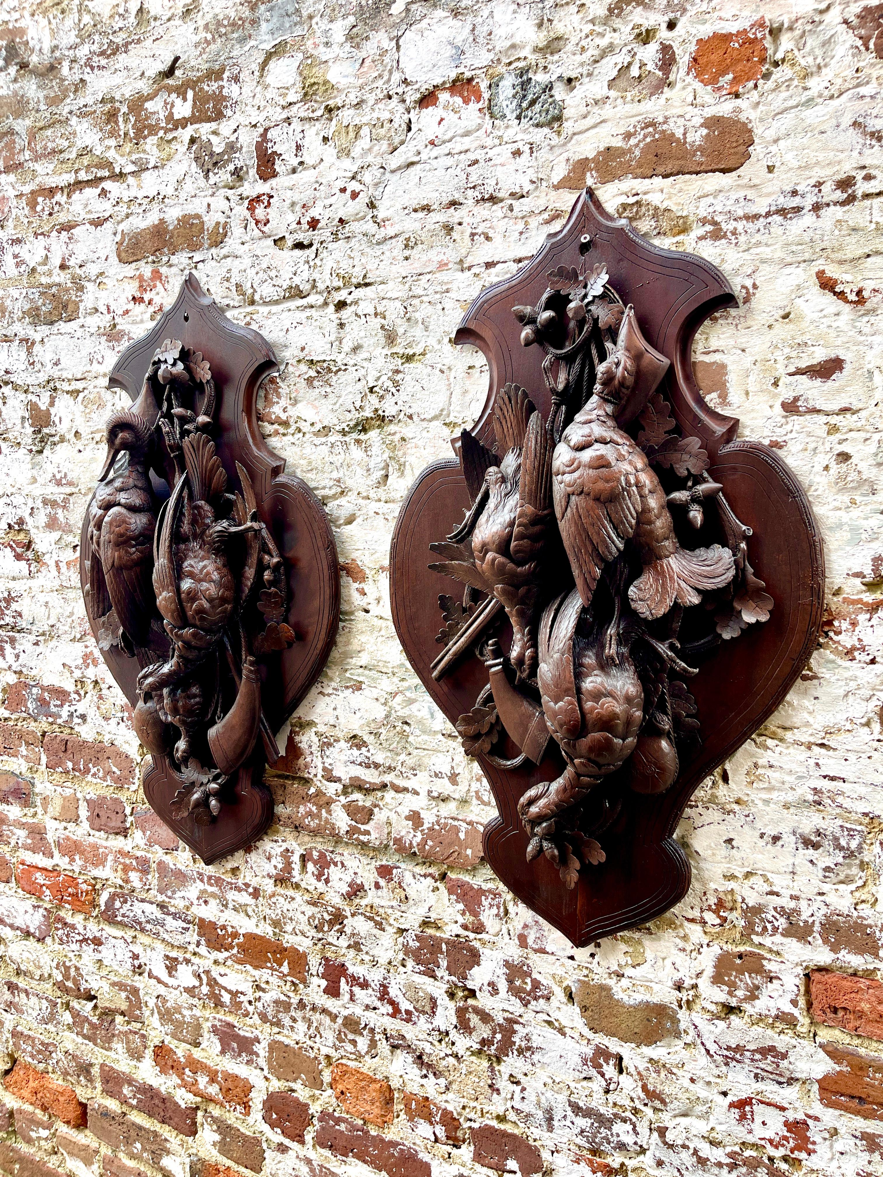 Pair of German Black Forest Game Plaques, 19th Century, wood carvings with trophies of game birds, powder horns, rifles and oak branches on cartouch shaped panel.