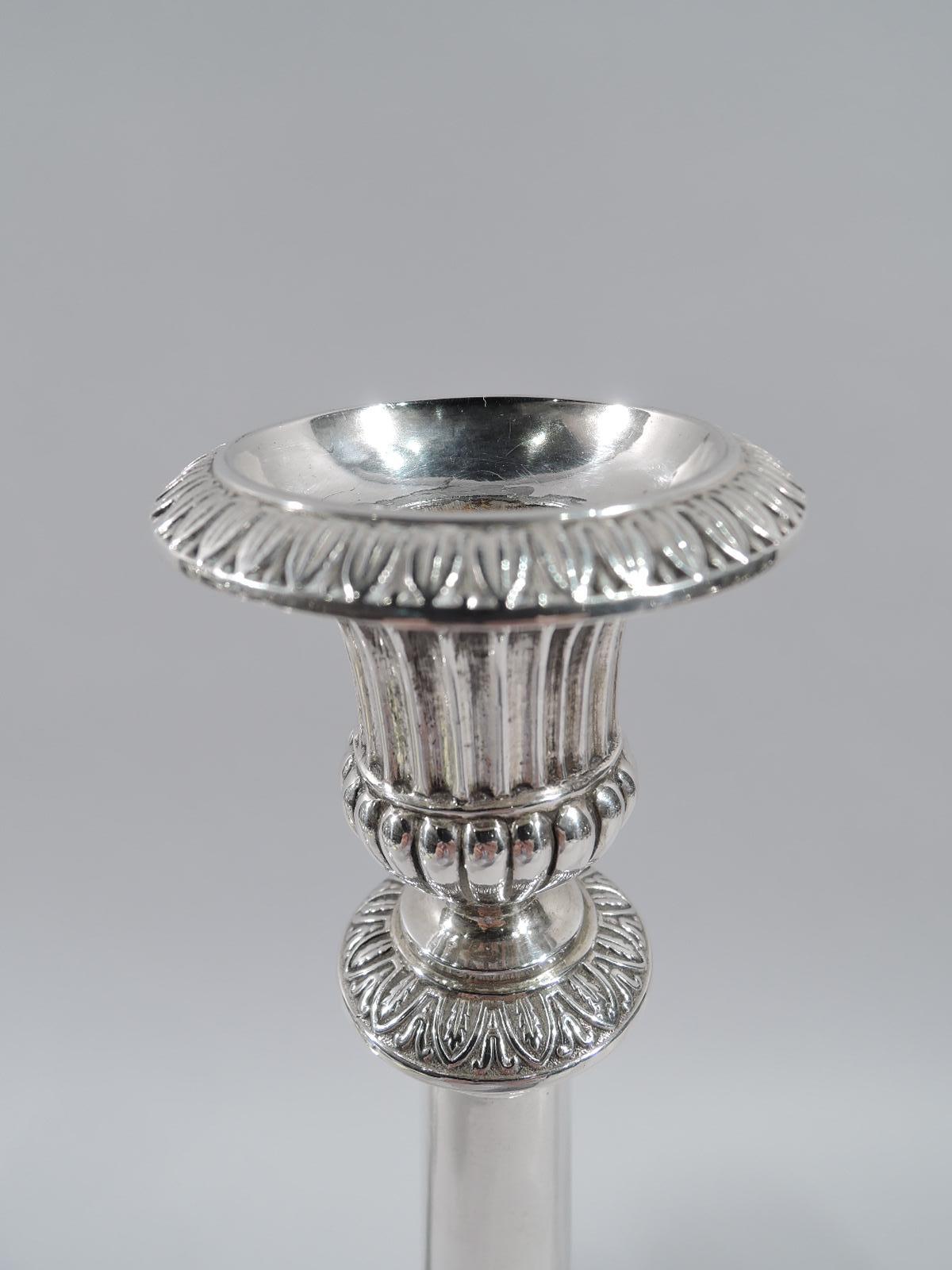 Pair of German Neoclassical silver candlesticks, early 19th century. Each: Upward tapering shaft on cylindrical plinth on stepped base. Bellied urn socket is fluted and lobed. Detachable bobech has leaf-and-dart ornament as do flange and foot rim.