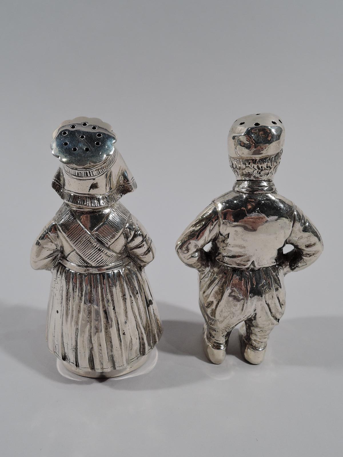 Pair of German 800 silver figural salt and pepper shakers, circa 1910. This pair comprises a boy and a girl. The boy wears baggy trousers and strikes a defiant pose with hands on hips. The girl, with shawl and apron layered over her gown, appears