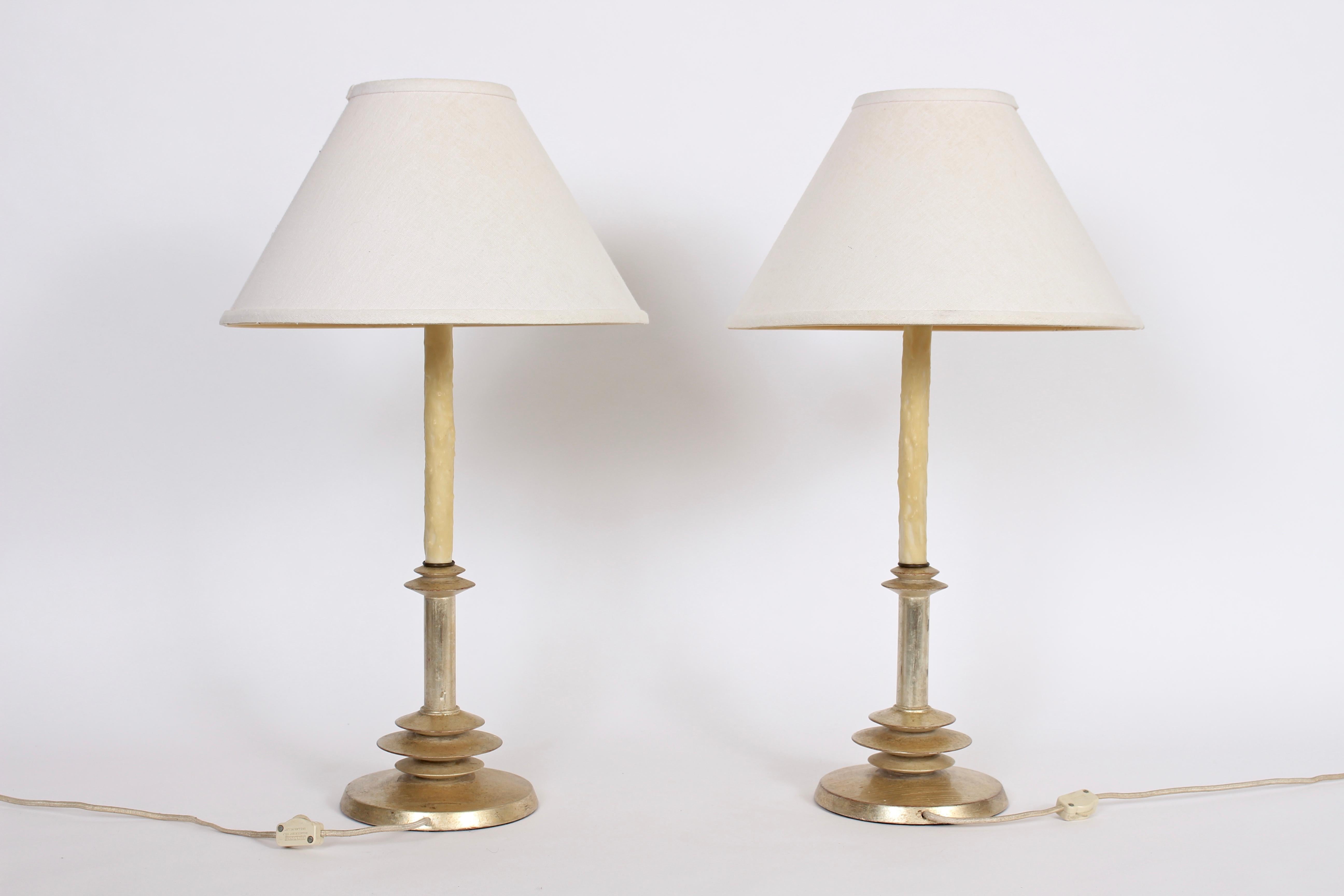 Hollywood Regency pair of Alberto Giacometti style gilt turned wood and waxed candlestick table lamps. Featuring a smooth turned wooden form, luxurious slivered antique gilding and creamed waxed candlestick column. Shades shown for display only (9 H