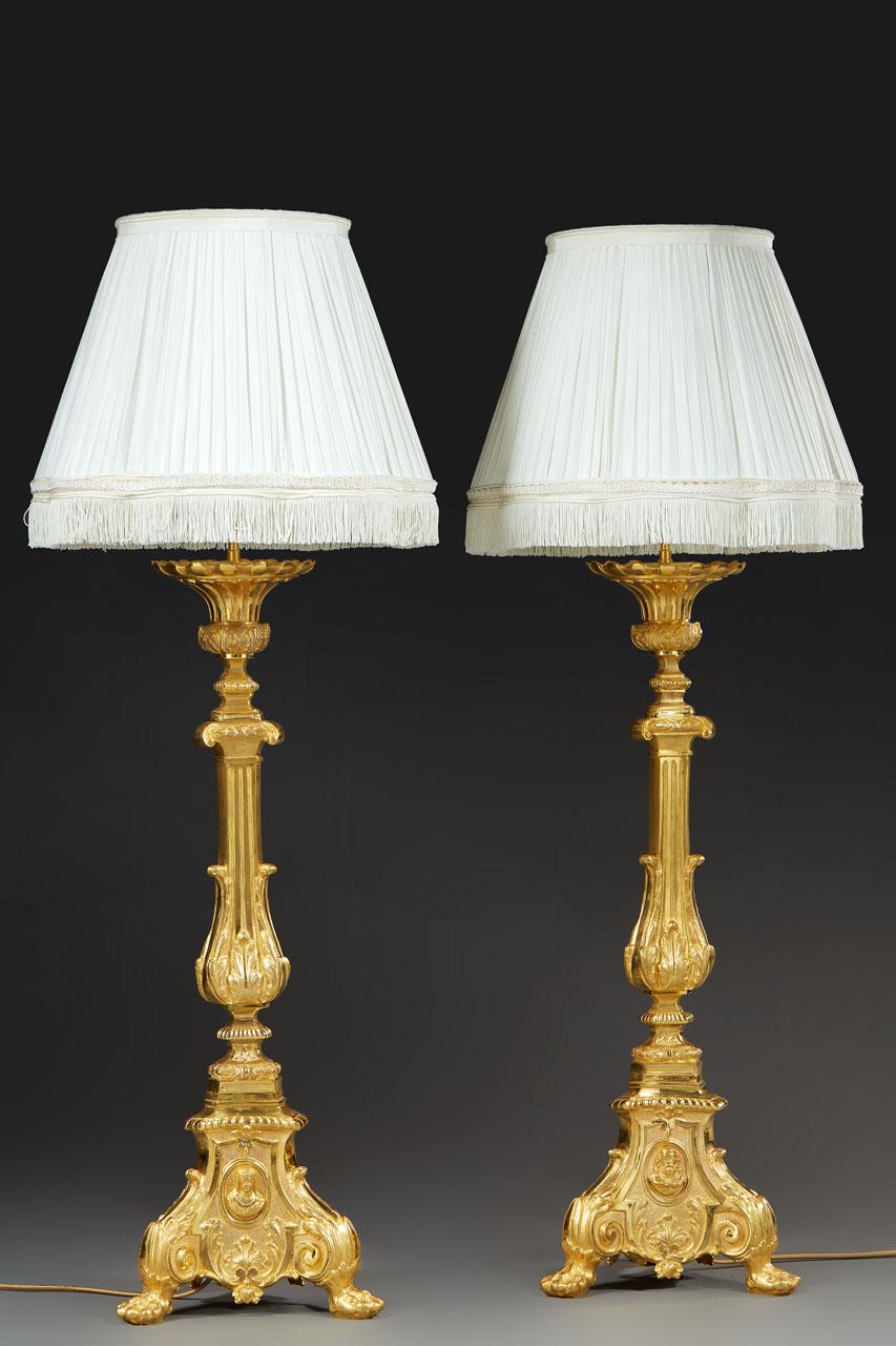 A pair of 19th century Louis XVI style carved and chased gilt bronze pikes-cierges, mounted as lamp bases. The fluted baluster base is punctuated by small cushions at mid-height, and rests on a tripod base ending in small claw feet. On each side of