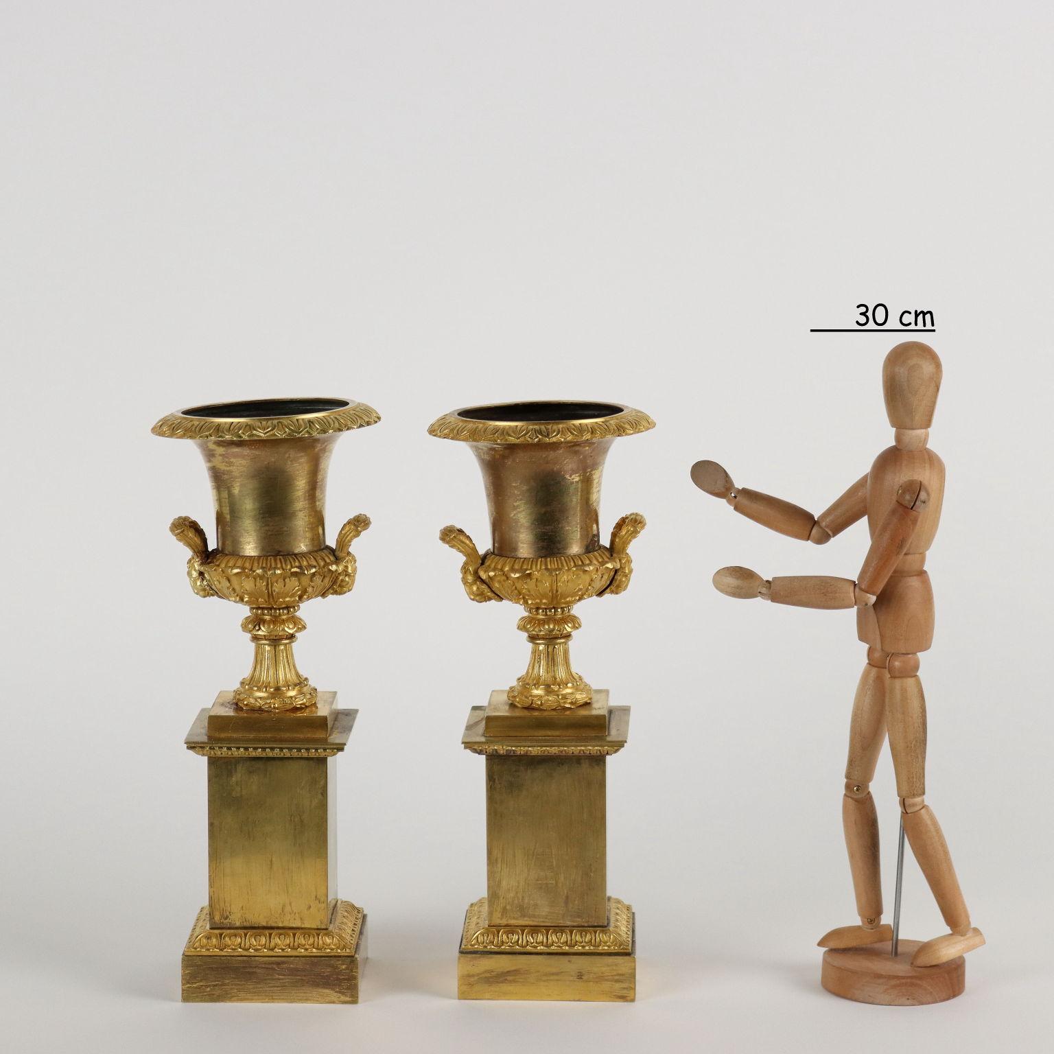 Pair of Medici vases in gilded and chiseled bronze with plinth base decorated with vegetable and Greek motifs. The two vases have two terminal handles with lion heads.