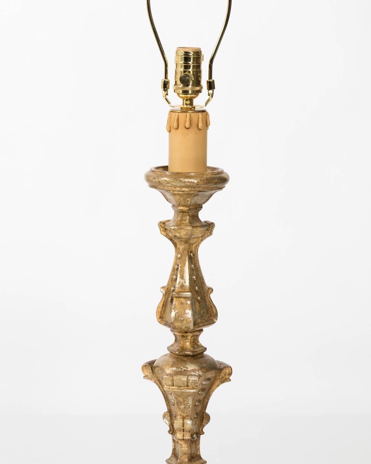 Pair of carved wood candlestick lamps in gold and silver gilt with new off white drum shades and finials, circa 1970s.