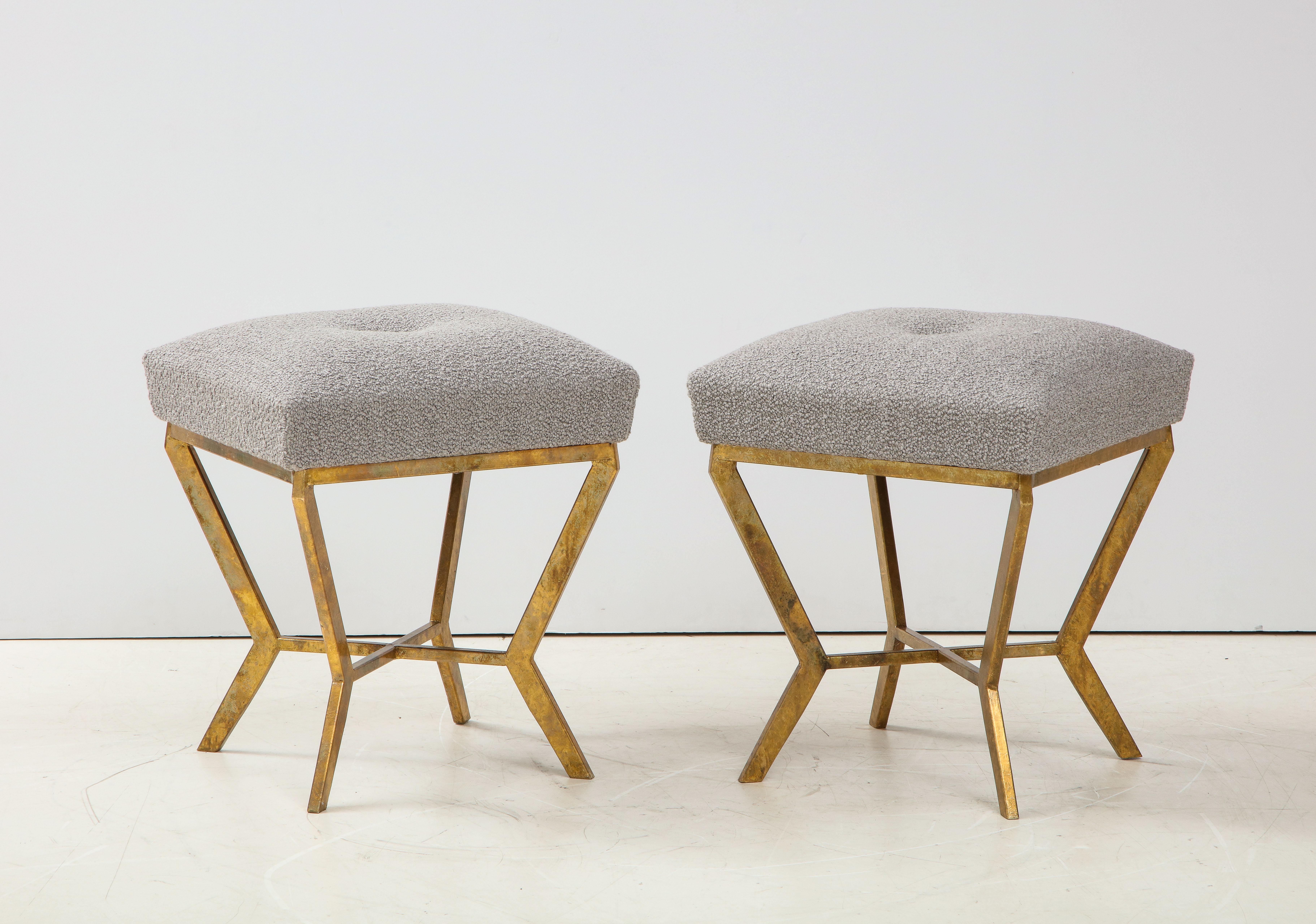 Pair of elegant iron stools hand-gilded with 24k gold leaf with a comfortable, one-button tufted seat upholstered in imported Grey tone boucle. Hand-made by master artisan in Florence, Italy. This pair of stools is on display at the Gallery at 200