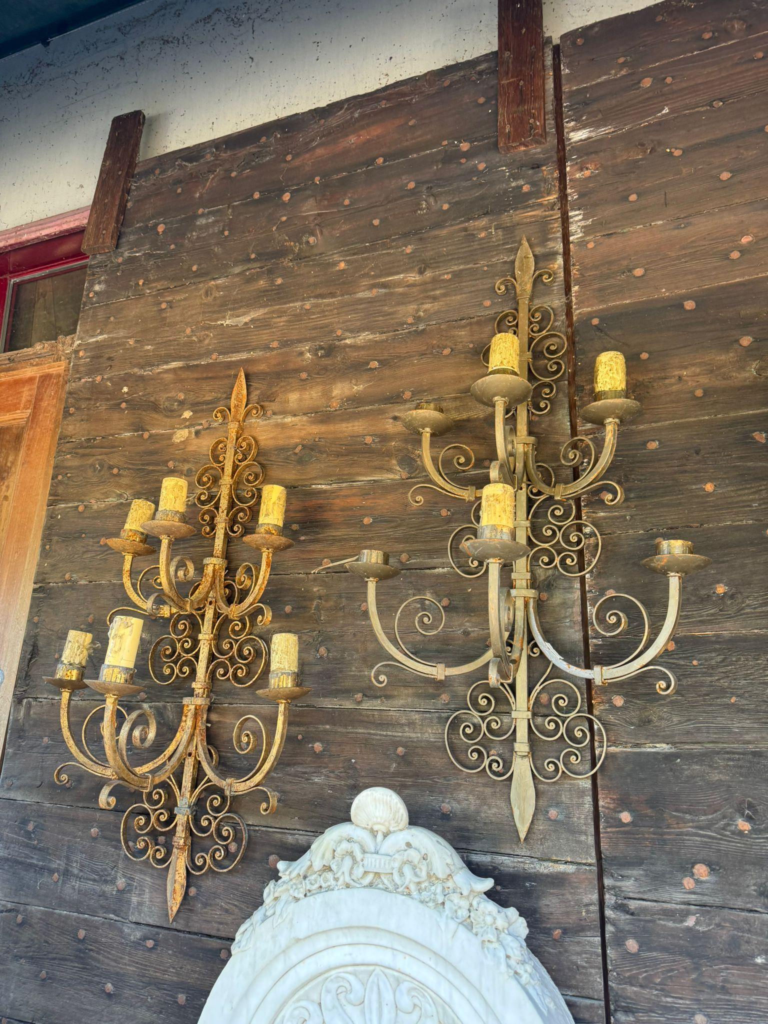 Antique vintage pair of wall sconces, made of gilded iron and decorated with curls and festoons, with two arms holding three lamps, for a total of six lights each. The electrification and lamp holders need to be checked. Original from the early