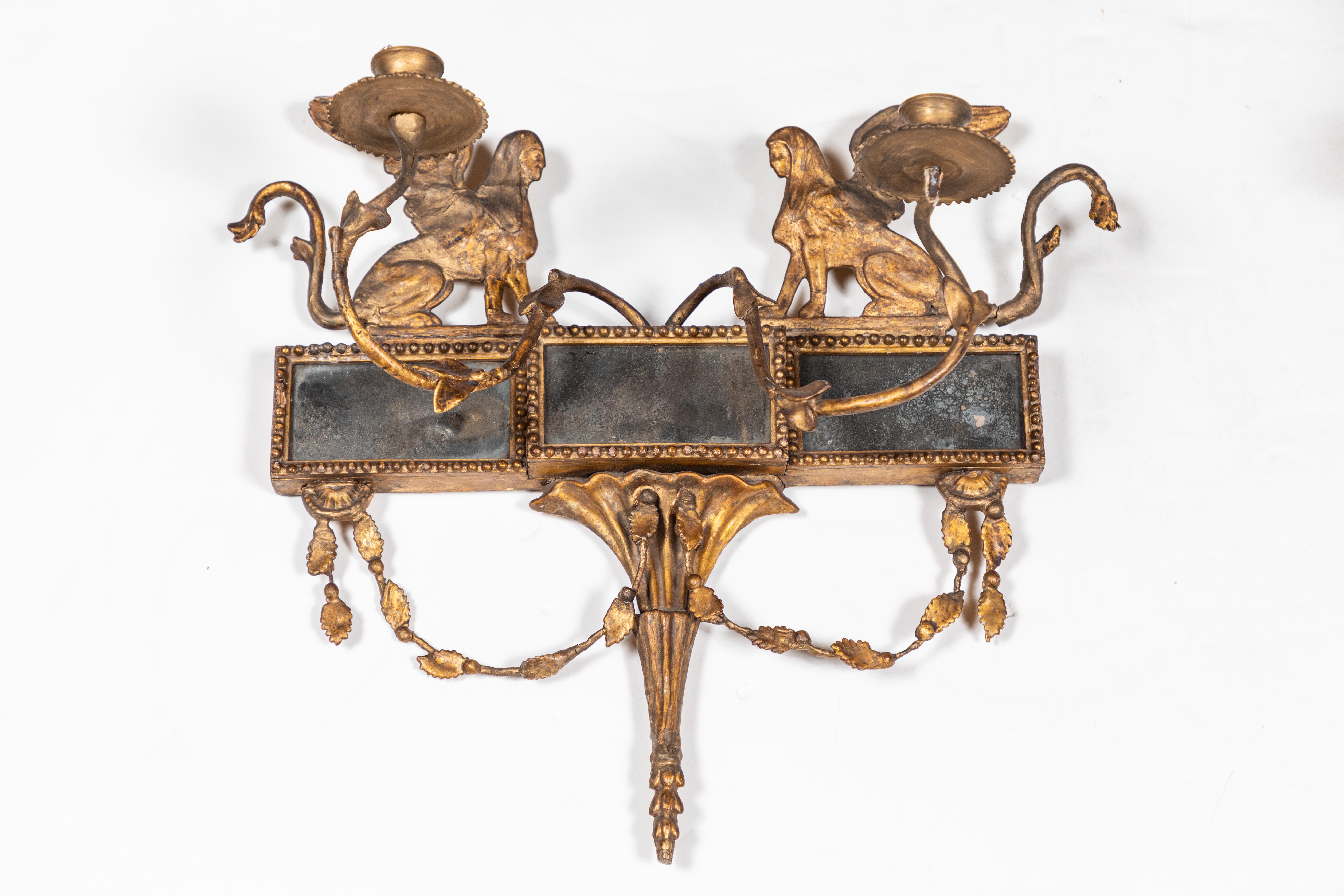 A pair of period, hand carved, gessoed, and 22-karat gold gilded, Second Empire, French sconces. Each with gilt bronze arms, and inset with original, mercury glass mirrors. Each with left and right facing, winged sphinxes above a torch-form base and