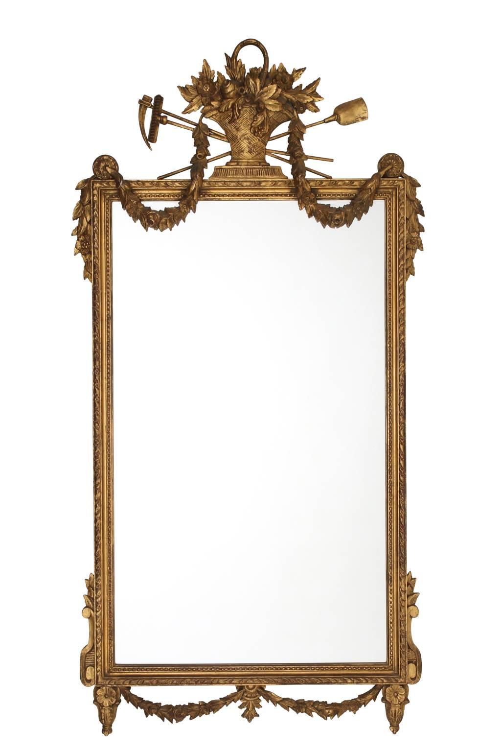 Pair of neoclassical style mirrors in gold gilt with a carved and decorated crown that features a basket of flowers and other garden harvest motifs, circa mid-20th century.
 
