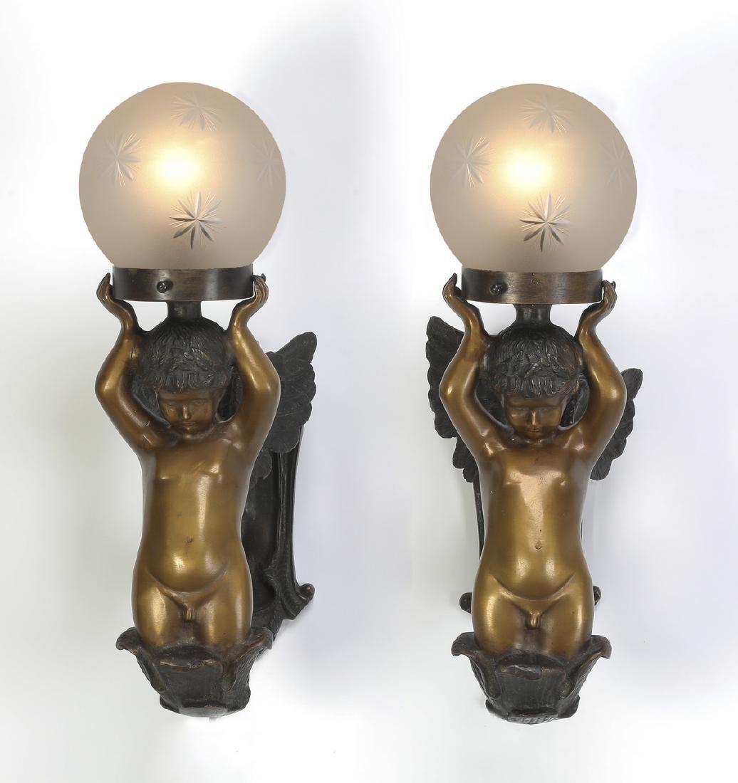 A pair of bronze cherub wall sconces from the Art Nouveau period. The classically formed cherubs are rising from waves holding illuminated neoclassical globes over head. Both are wired with plugs. The globes are frosted with diamond shapes etches