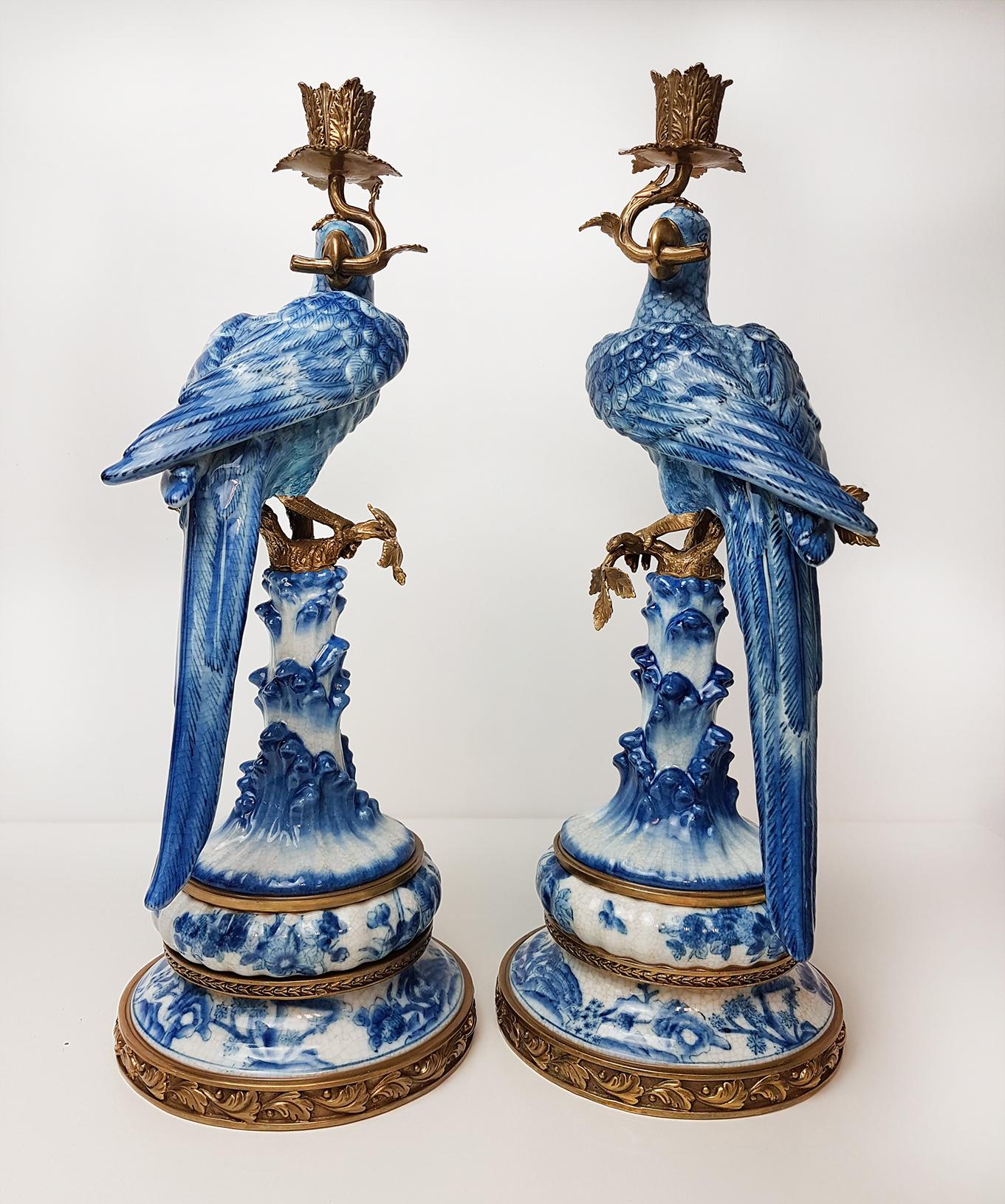 20th century pair of gilt bronze based porcelain pair blue and white parrot candlesticks.
Beautiful hand painted, left and a right orientated parrot candlesticks, almost identical.

The parrots hold bronze 
