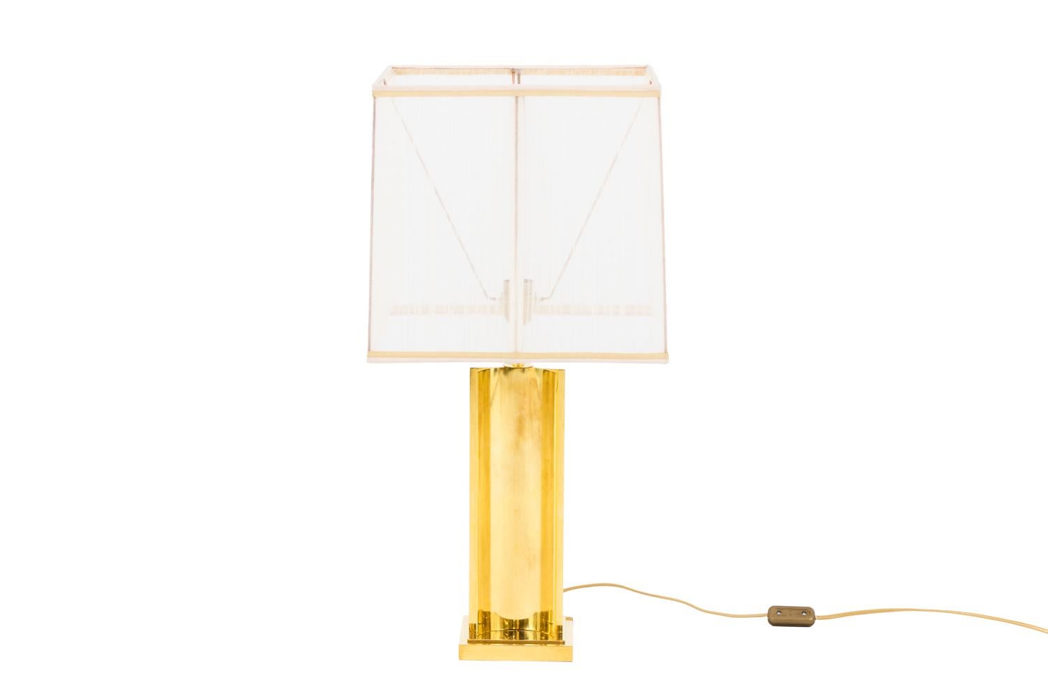 Gilt brass lamp with a shaft in three half-tubes shape backed around a central round stick.
Molded square shape base.

Square lampshade in white organza.

Work realized in the 1970s.

New and functional electrical system.

! The price doesn’t