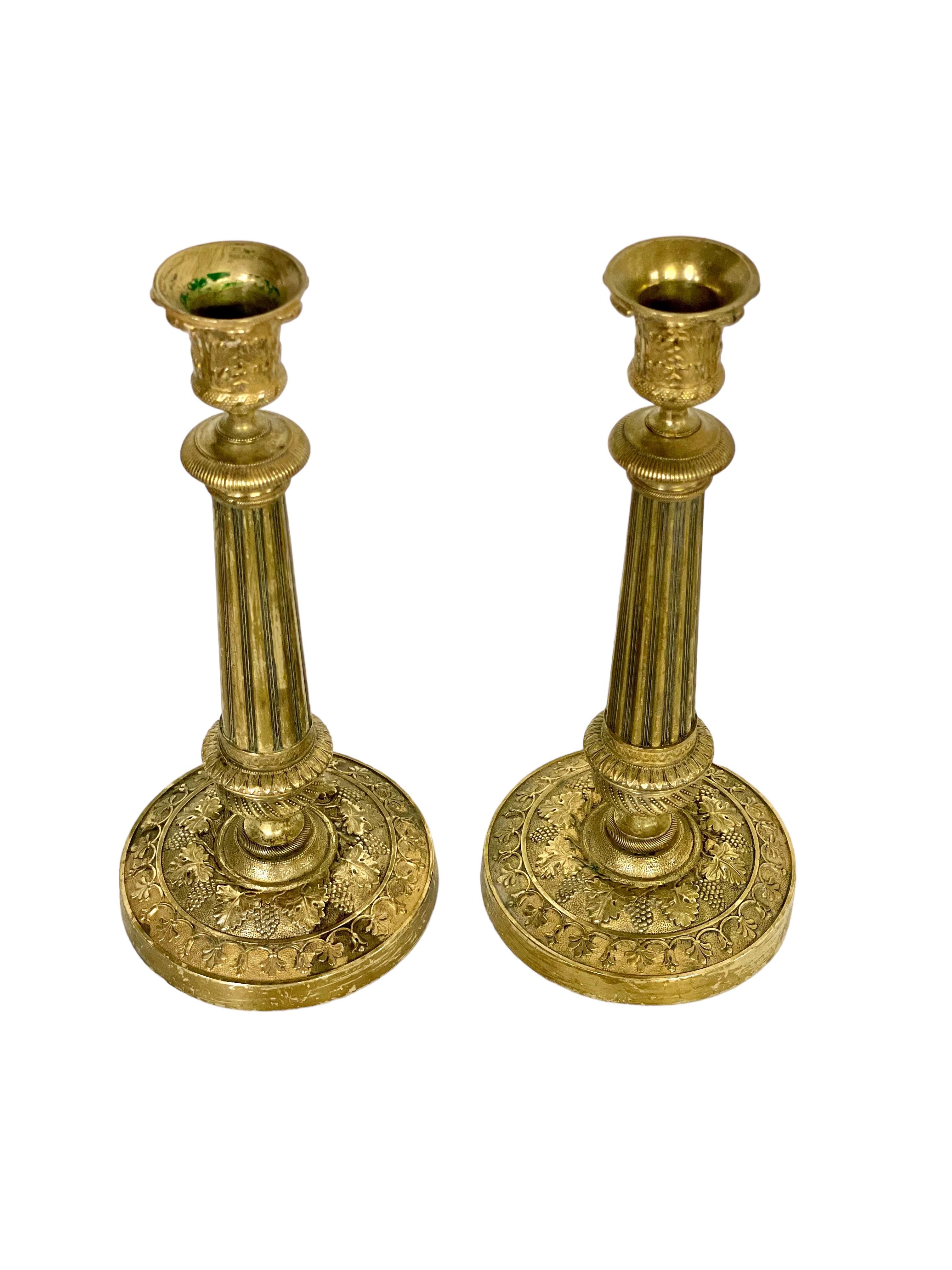 A pair of very finely-chiselled French gilt bronze candlesticks crafted in the neoclassical style. The decoration is extremely intricate, particularly on the circular base and tulip-shaped capitals, with encircling bands of grapes and vine leaves,