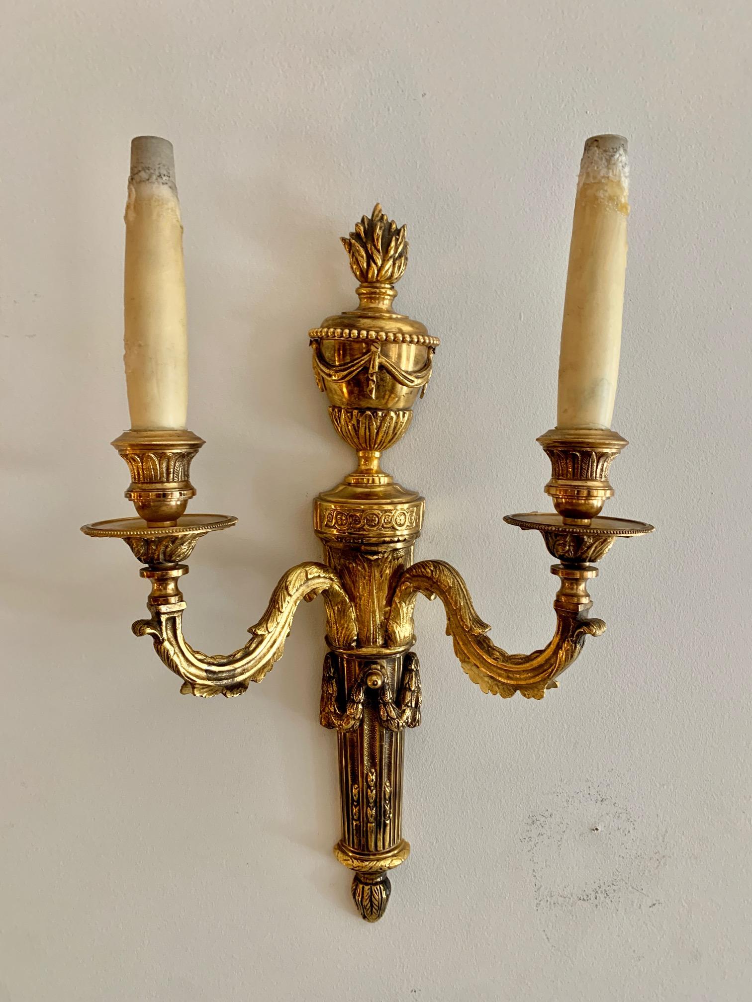 Pair of French Louis XVI style 20th century gilt bronze dore with two arms and center torch, urn and brazier finail decorating the top, acanthus feal detail an arms and neoclassical ornaments, They are electrified and ready for use, the candles are