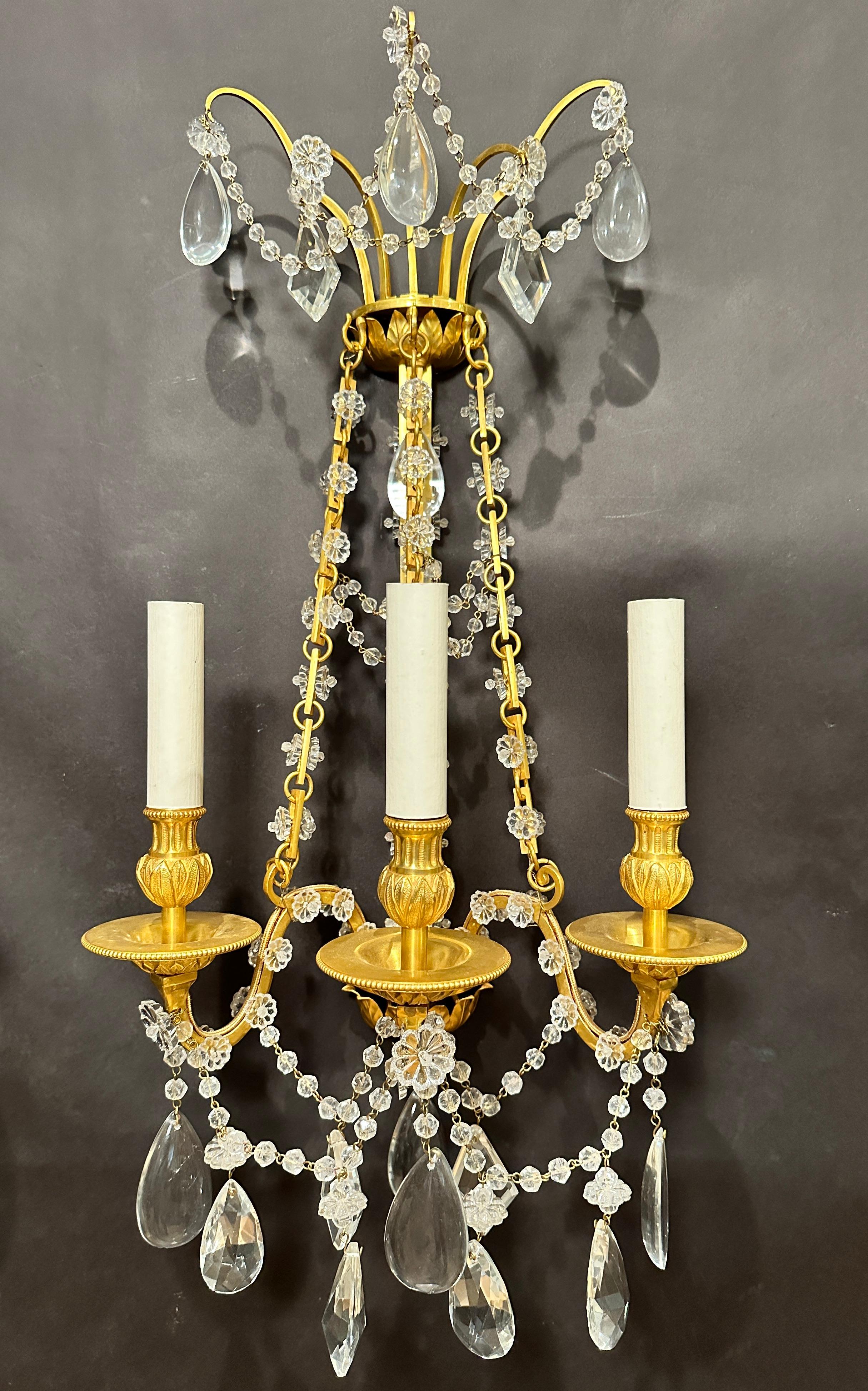 Fino par de apliques franceses de bronce dorado y cristal de estilo neoclásico con influencia de Luis XVI. Guirnalda drapeada de cristal y bronce entre tres brazos.