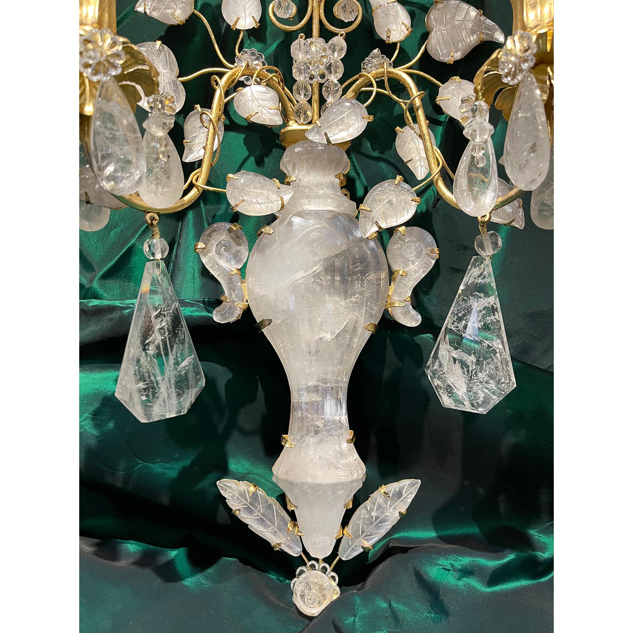 An exceptional pair of two light cut crustal sconces with gilt bronze armature. The anchor of the piece is it's central rock crystal vase with scroll form handles. Rock crystal leaves with carved veins and flowers with individual crystal petals