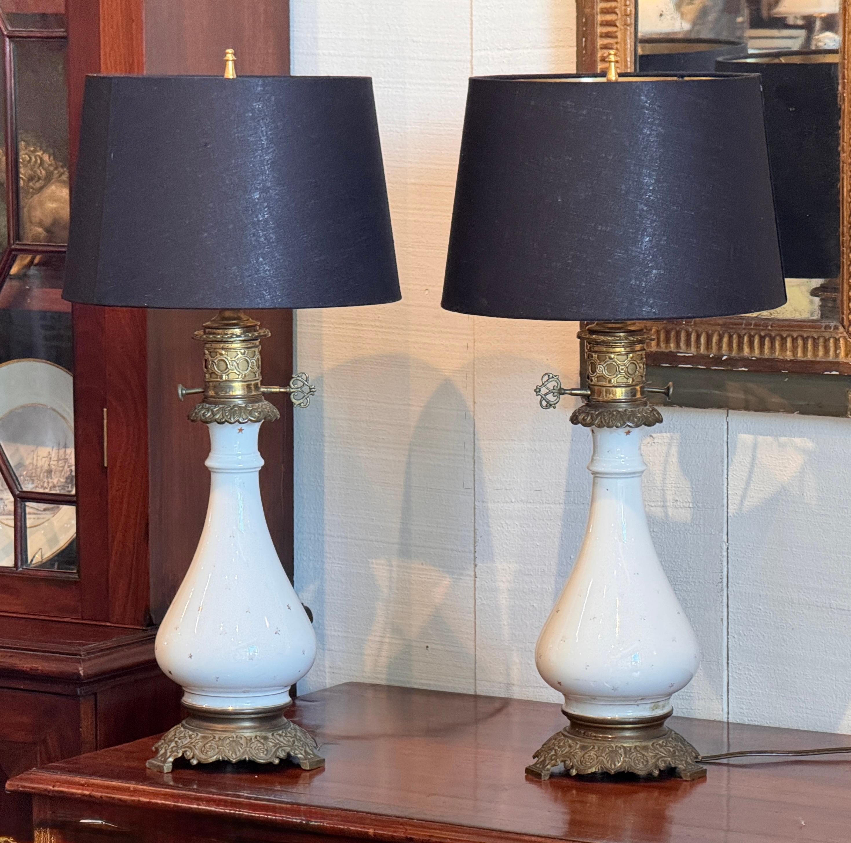 A pair of white opaline glass lamps with ornate gilt bronze mounts, including finely cast bases and collars. Each lamp features a classic teardrop form decorated with delicate gold stars, paired with intricate pierced bronze galleries and original