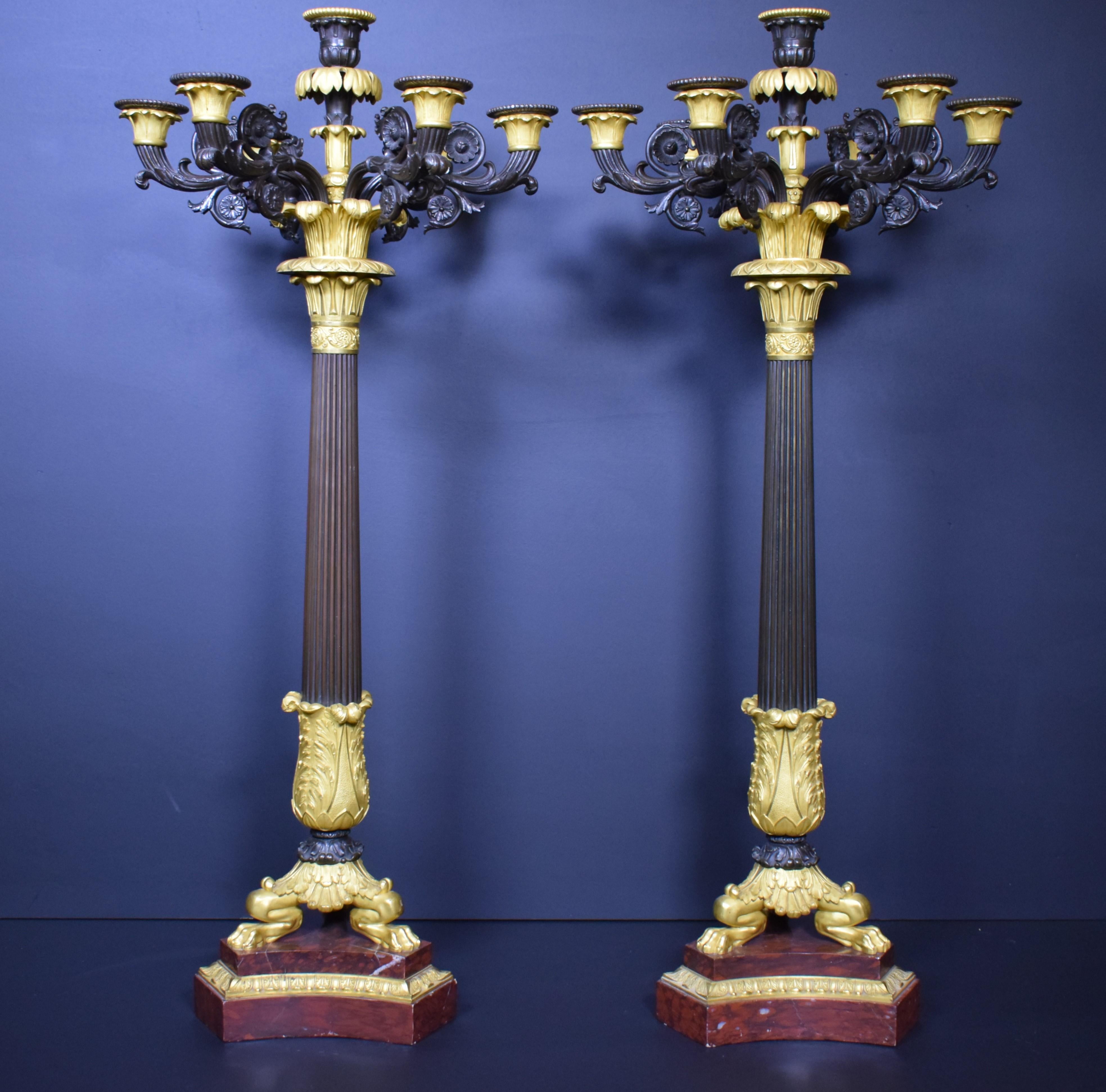 French. Pair of gilt bronze and patinated bronze neoclassical style seven light candelabra having column form, paw feet and raised on a Rouge Griotte marble step plinth. Apparently unmarked. Measures: Approx. H. 36.25