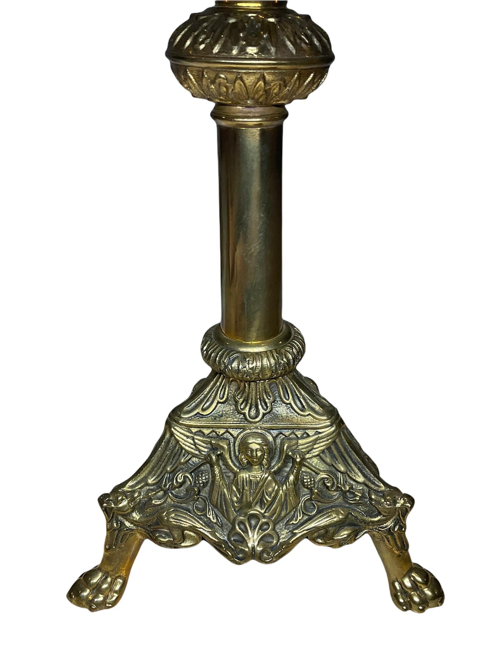 This is a pair of heavy gilt bronze church altar candle holders. They are decorated by repousse angels, bird-dogs figures and pine cones at their triangular bases. There are also some chased feathers, leaves and flower motifs adorning the candle