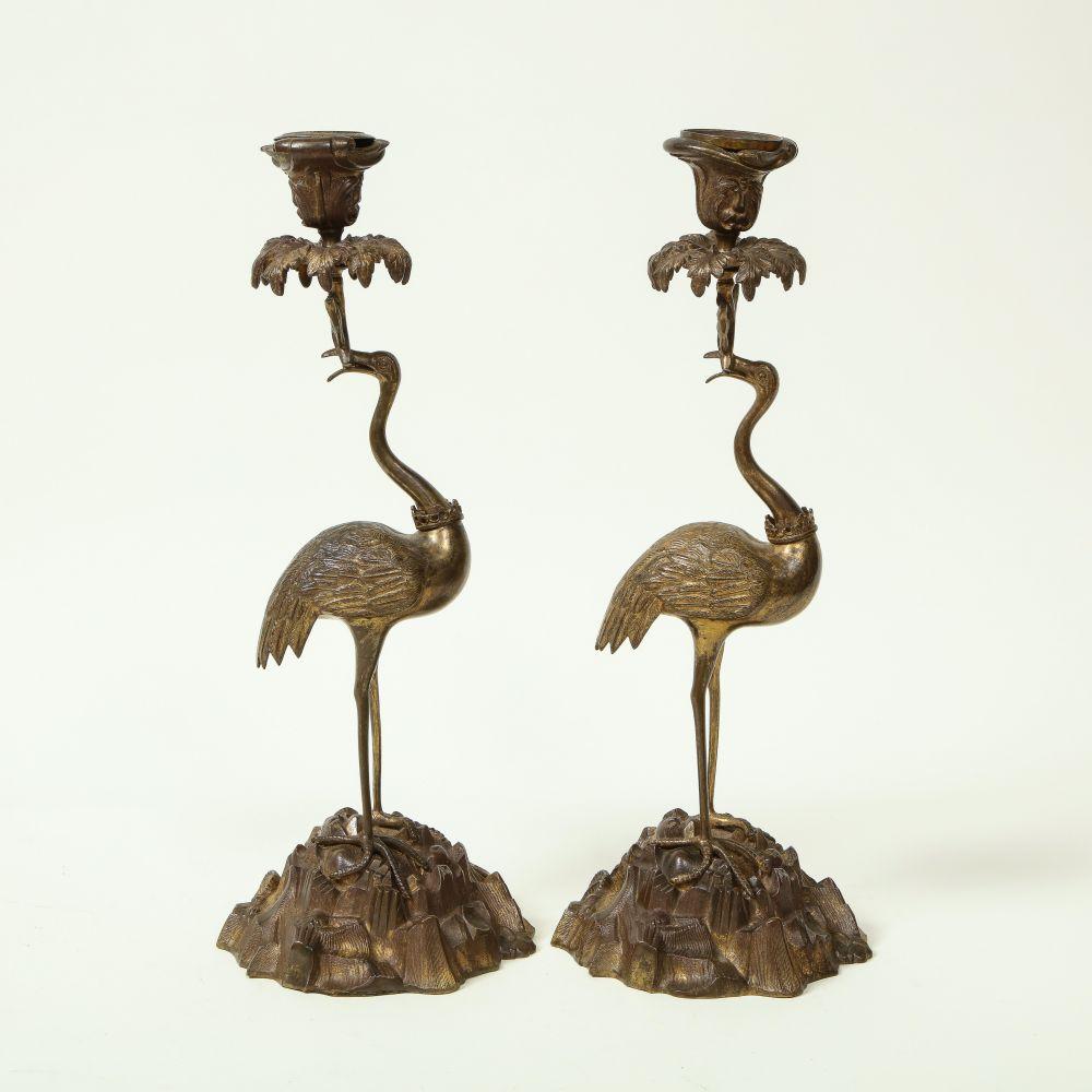 Each in the form of a bronze ostrich on a rockwork base; supporting a candleholder. 