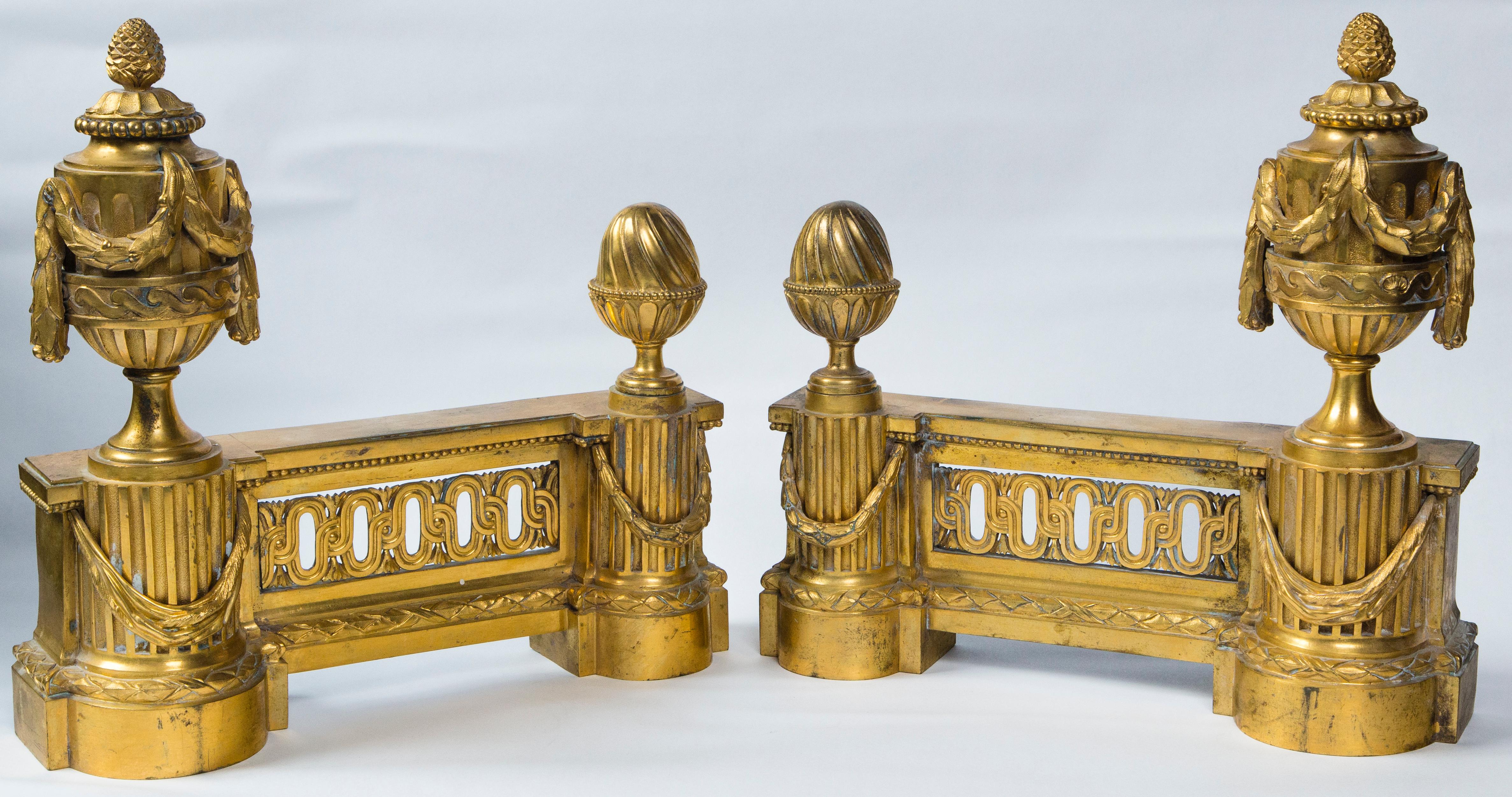 This pair of beautifully crafted chenets, retain their original mercury gilding. Two half round fluted columns, at either end. Each column decorated with an applied swag and topped by a knob finial on one and an acorn finial on the taller. A 