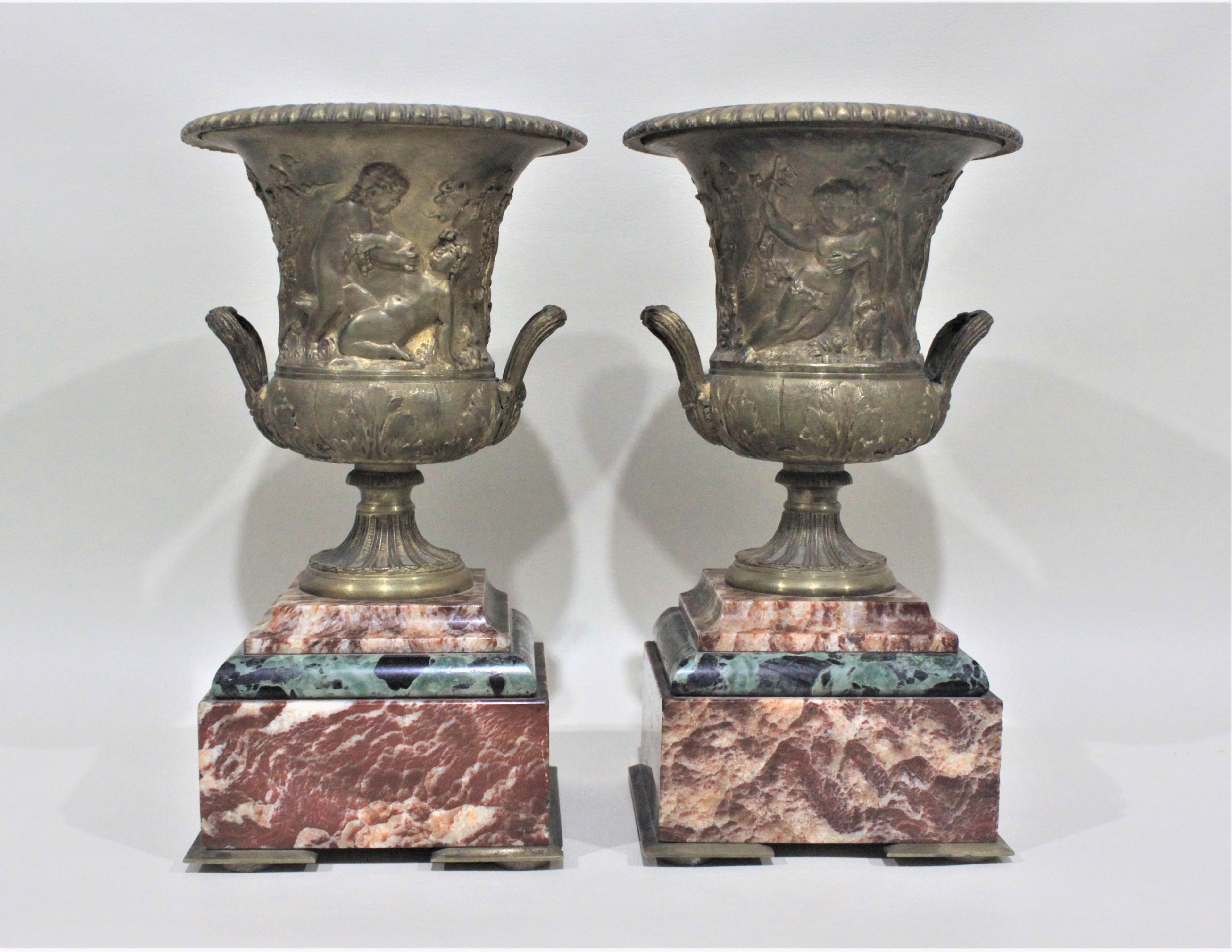 This pair of gilt bronze and marble urns or garnitures are ornately cast with a Neoclassical motif on both the front and back which sit on a base of alternating pink and black polished marble slabs. This matched pair of urns likely date from the