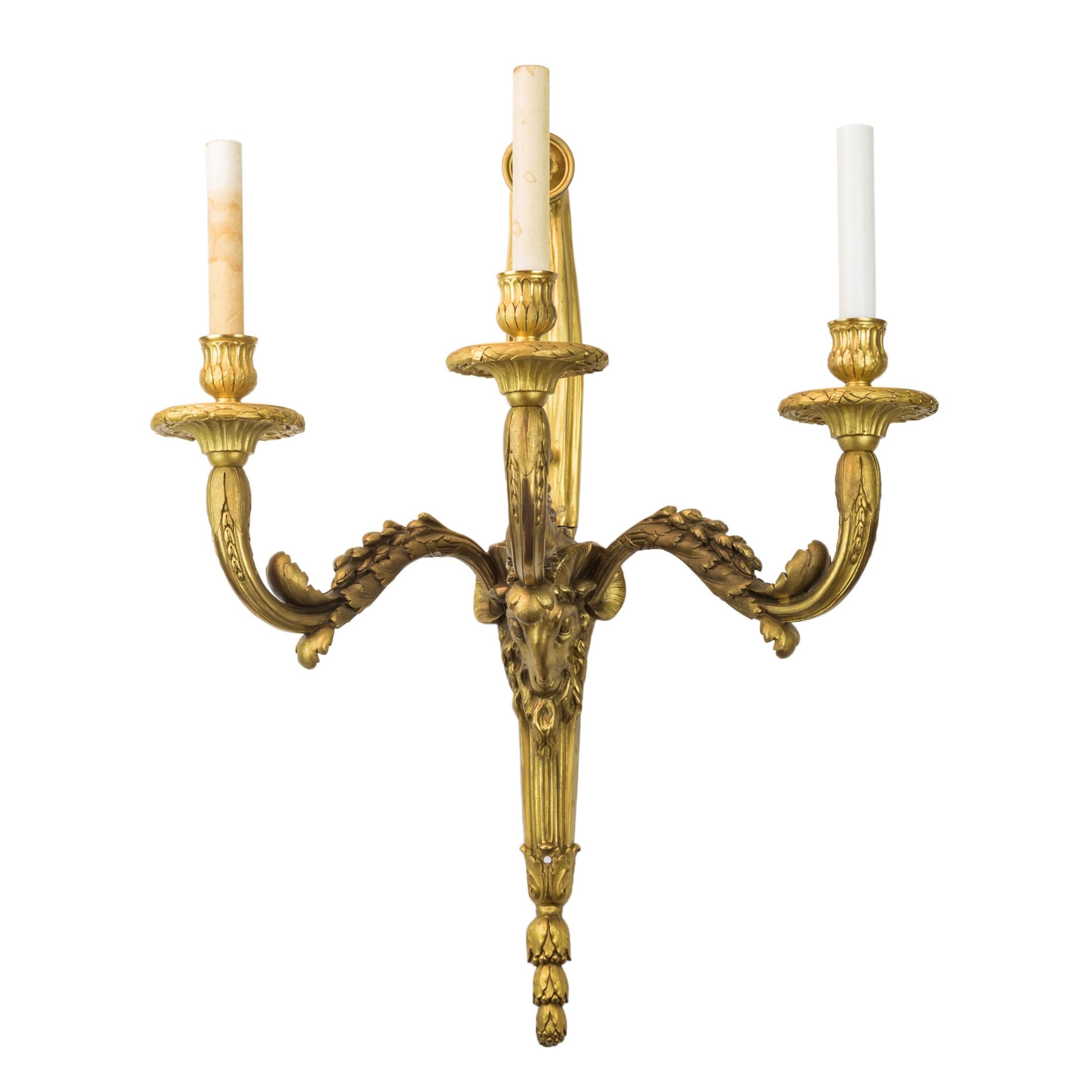 Pair of high quality gilt bronze three-light sconces
each cast with a ram's head mask issuing curved leaf cast candle arms. The ribbon tied backplate hung with finial pinecone.

Origin: French
Date: 19th century
Dimension: 24 in (H) x 19 in (W)