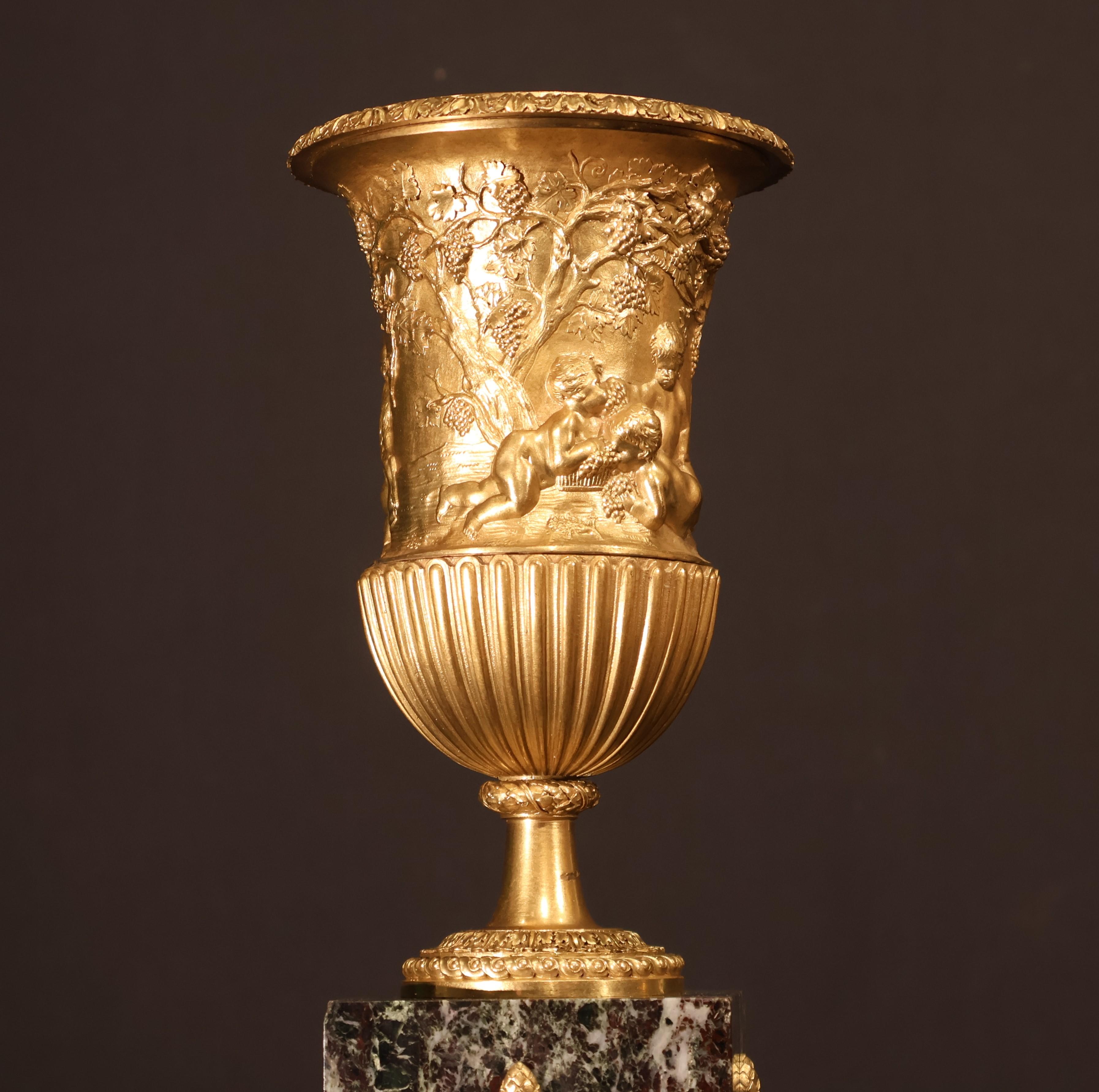 Gilt Pair of gilt bronze urns raised on a marble plinth with ormolu mounts.  For Sale