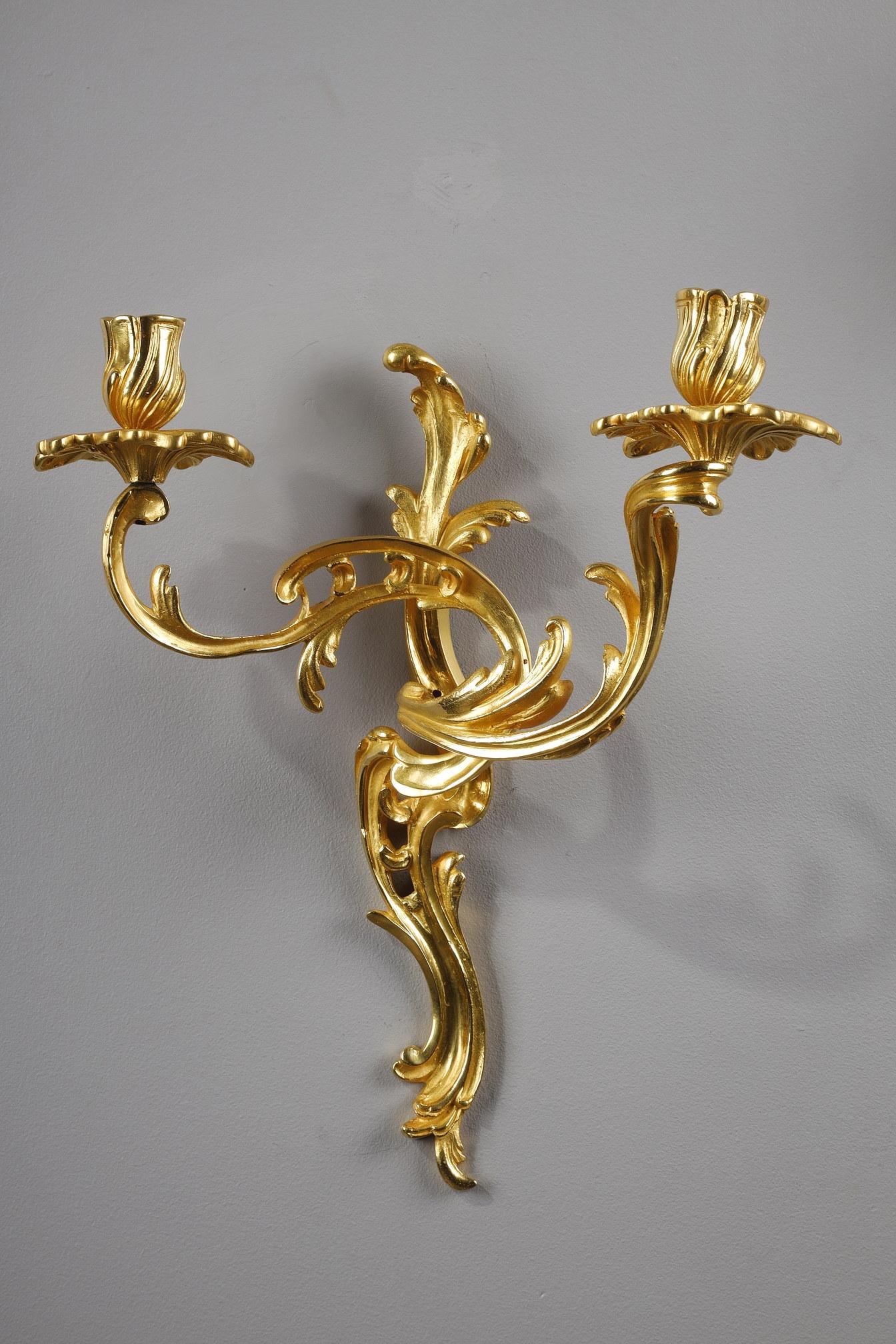 Pair of ormolu candlesticks with two arms of light in Louis XV style. With their decorations of moving foliage, these candleholders are typical of the Rocaille style. The binnacles are treated like flower buds with leaves. 

This reinterpretation
