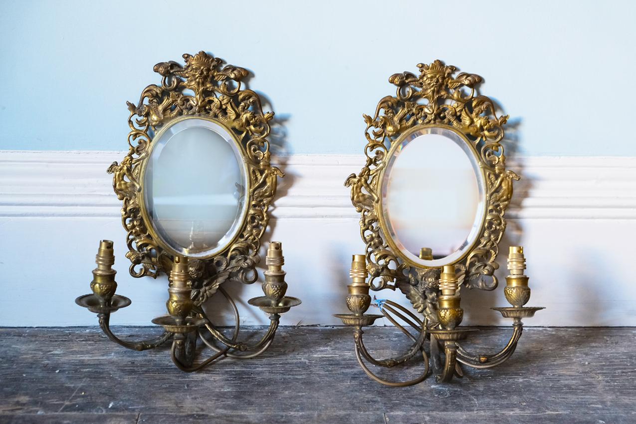 A pair of neoclassical style gilt carved and mirrored wall sconces, each with three candle branches.