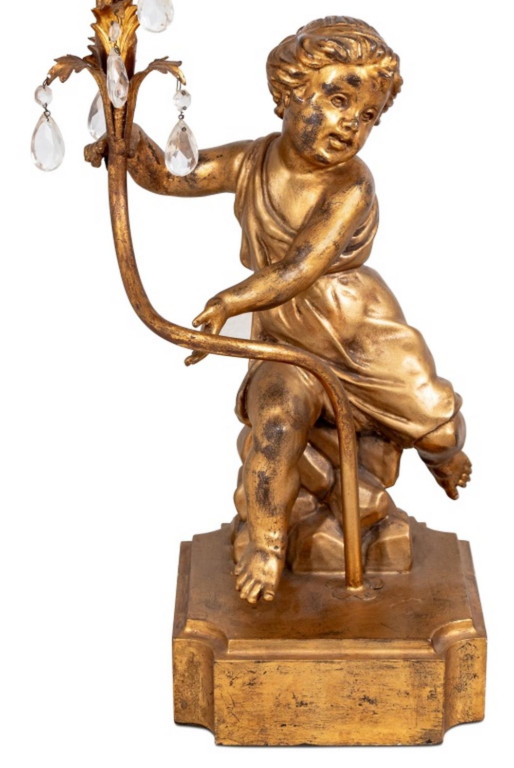 Pair of Gilt Composition Cherub Five Branch Lamps, 20th century, each with a draped cherub seated on rockwork upholding a foliate stem issuing five branches with cut glass prisms. 39.5