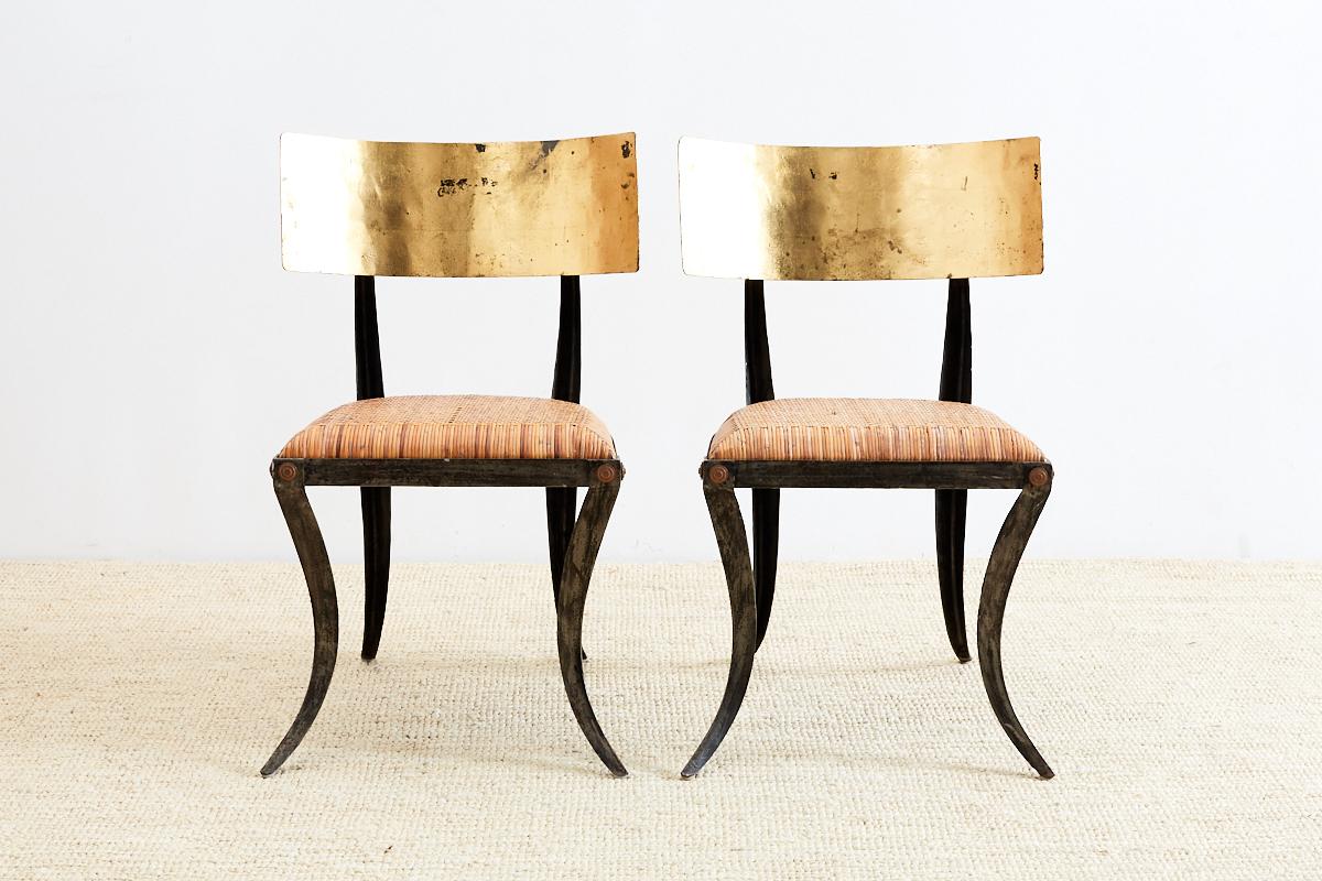 Fantastic pair of iron Klismos chairs featuring a woven rattan seat. Each chair is decorated with a gilt seat back made from squares of gold leaf hand-applied with a rich, vintage finish. The frames have dramatic curved legs with gold medallion