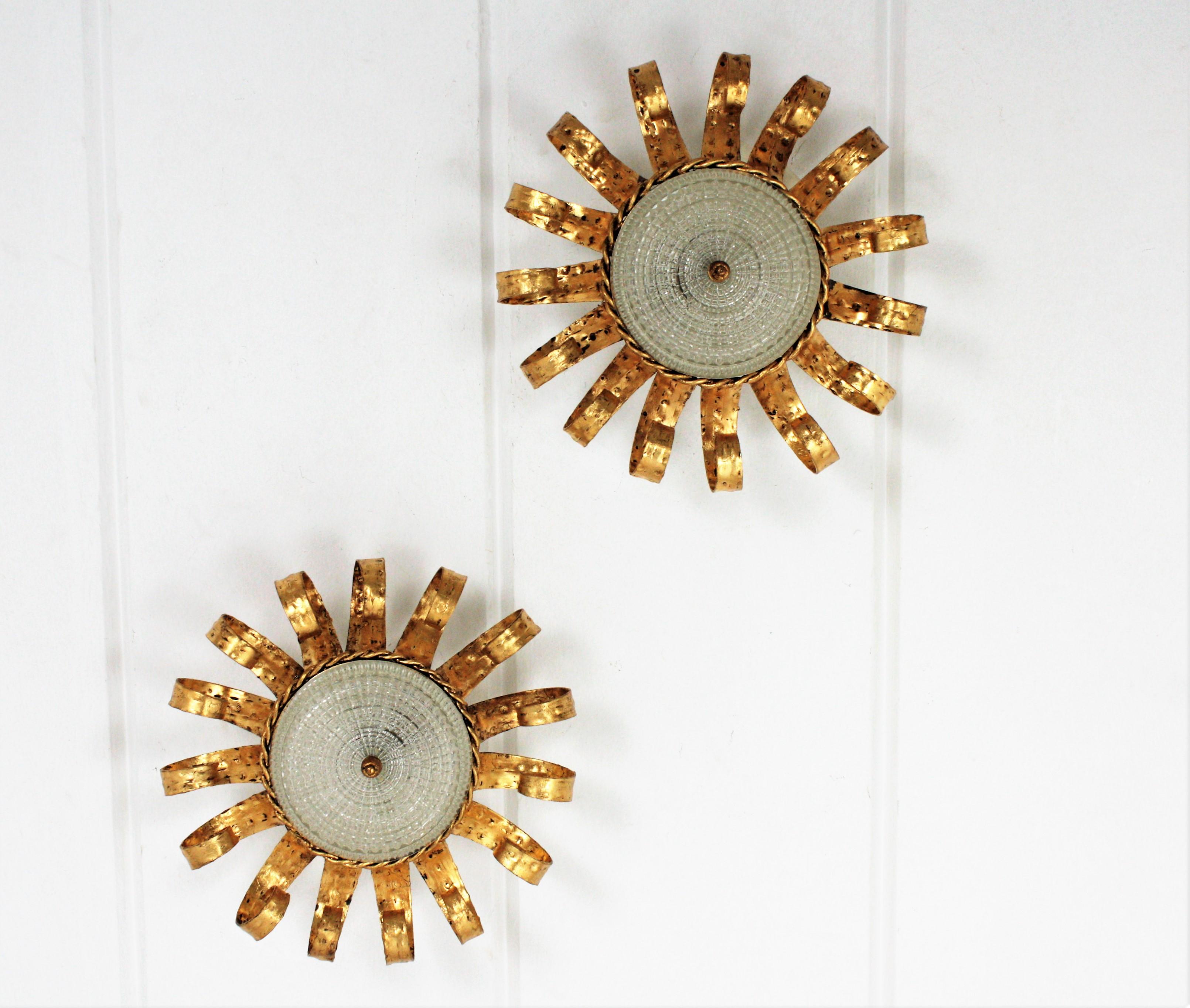 Pair of Brutalist hand-hammered iron sunburst crown light fixtures with scrolled frames, central glass pressed shades and gold leaf finish.
Spain, 1960s.
The structure is heavily adorned by hand-hammered scroll work with gold leaf gilding and curvy