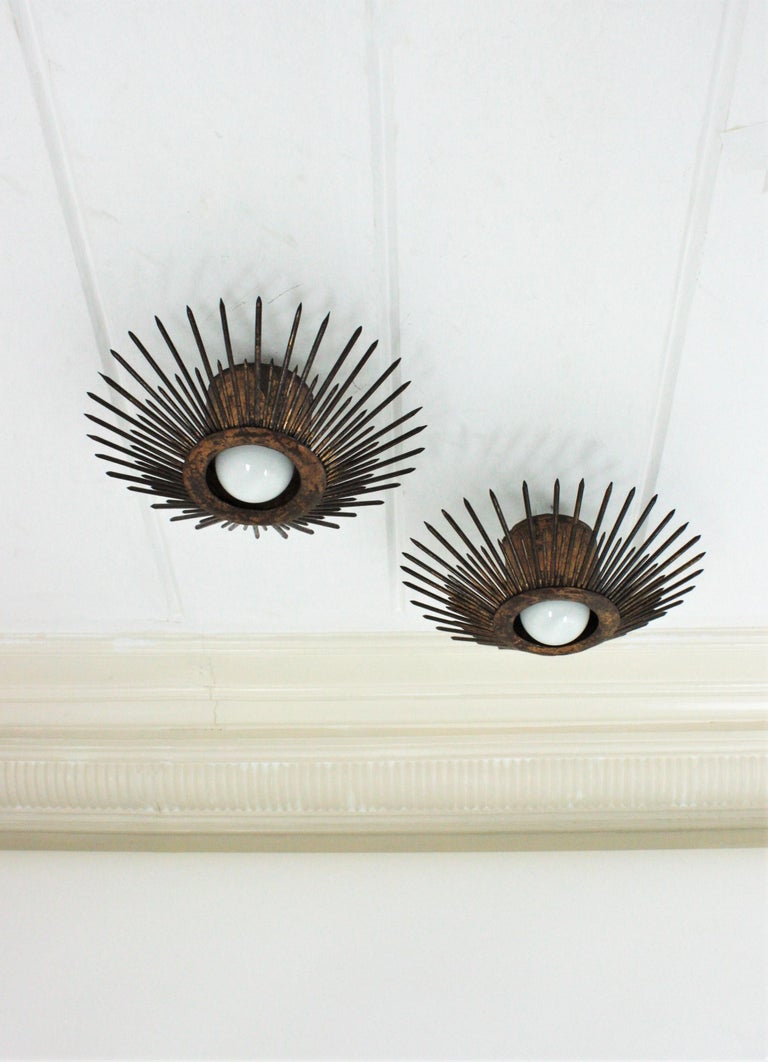 Terrific pair of wrought iron sunburst flush mounts with spikes design and parcel-gilt finish. France, 1940s.
These eye-catching sunburst ceiling lights have a strong design with pointed spikes in sunburst disposition. They have two layers of iron
