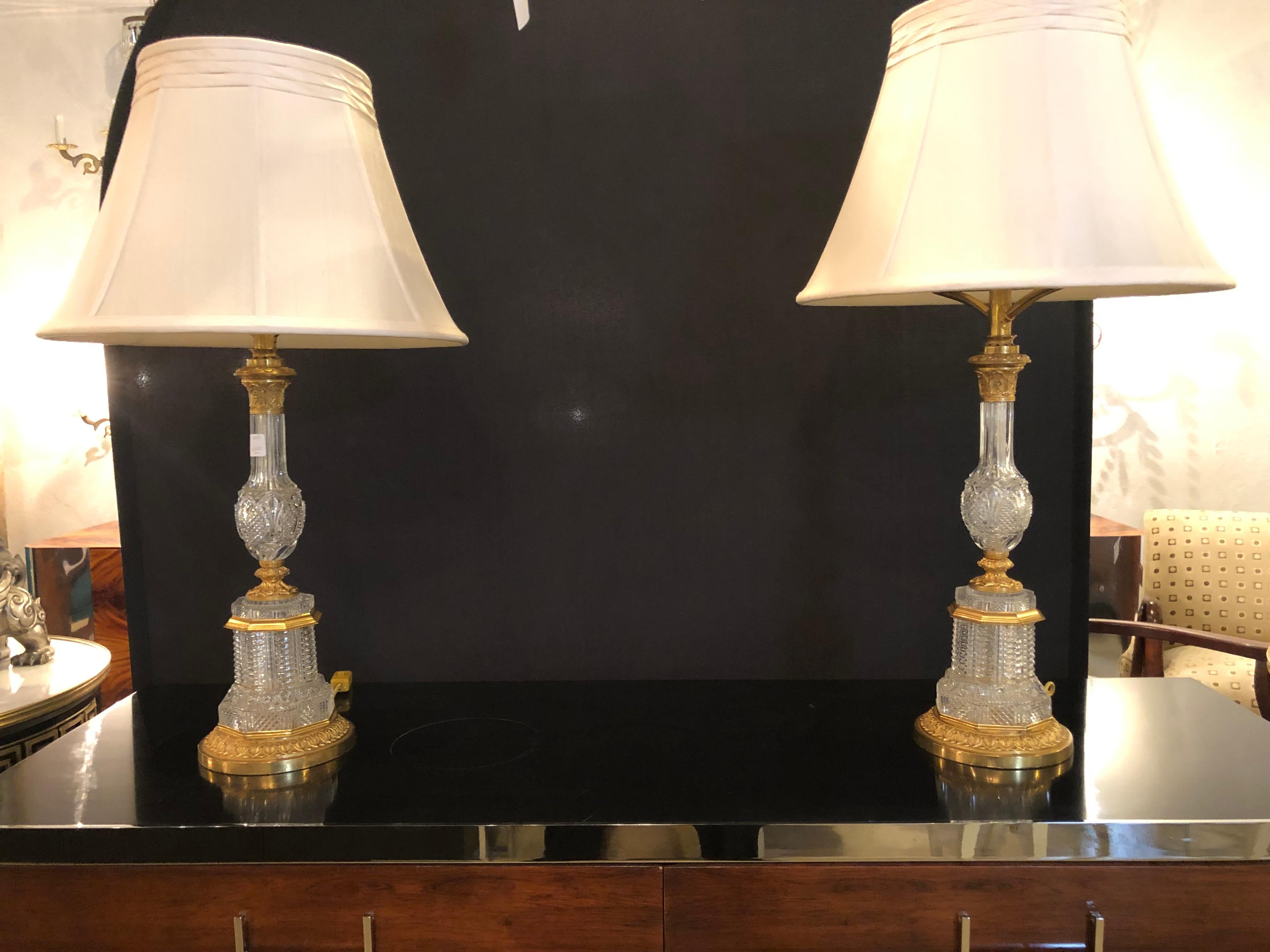 A large and impressive pair gilt metal finely cut crystal antique oil lamps converted into table lamps each having custom shades. This pair of very finely cut crystal old oil lamps have been redone into table lamps. The crystal having very fine gilt