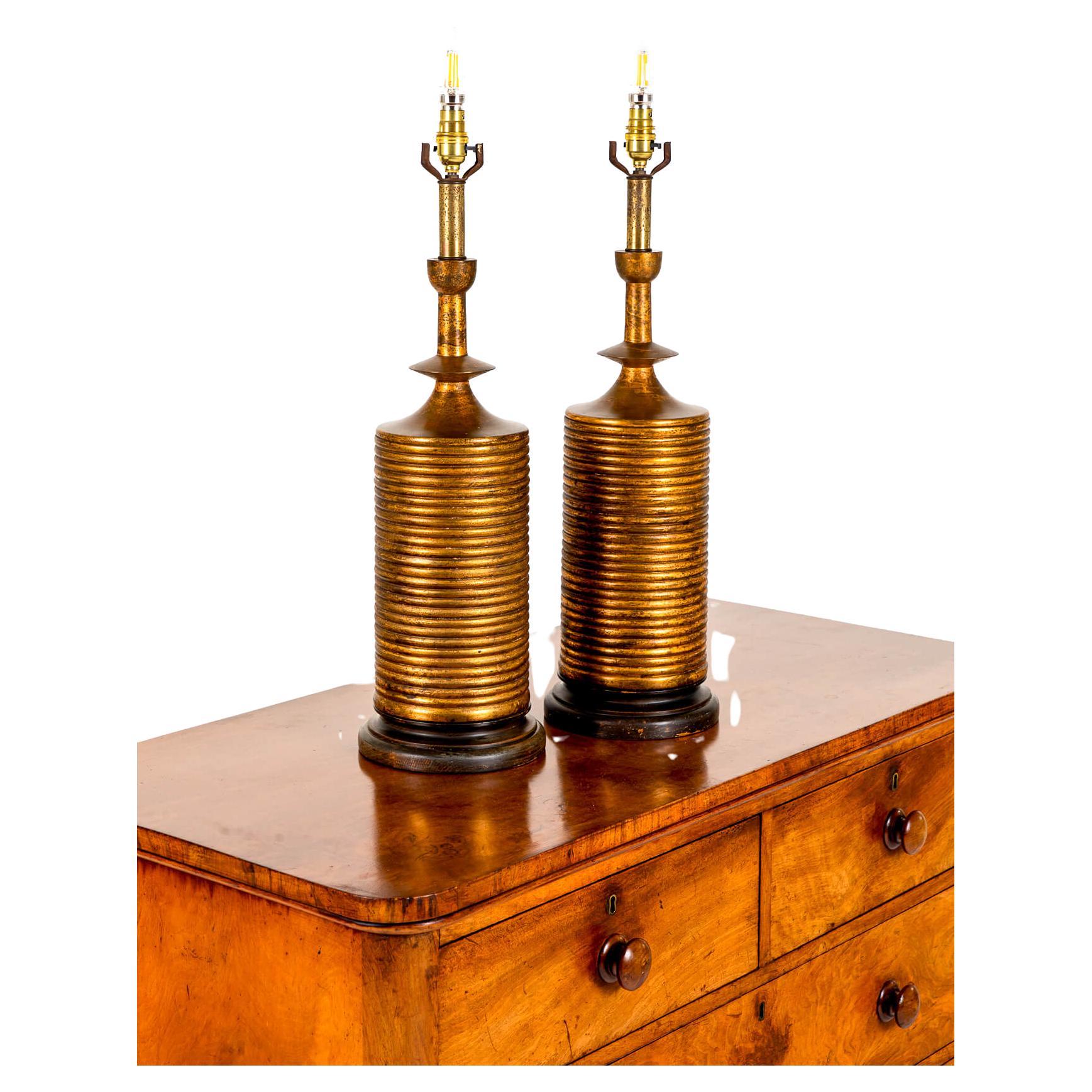 Une magnifique paire de lampes de table dorées provenant d'un domaine de Cornouailles.

Bases en bois tourné sur des colonnes circulaires cerclées de doré avec des tiges cannelées de couleur laiton.

Les lampes ont été restaurées et conservent une