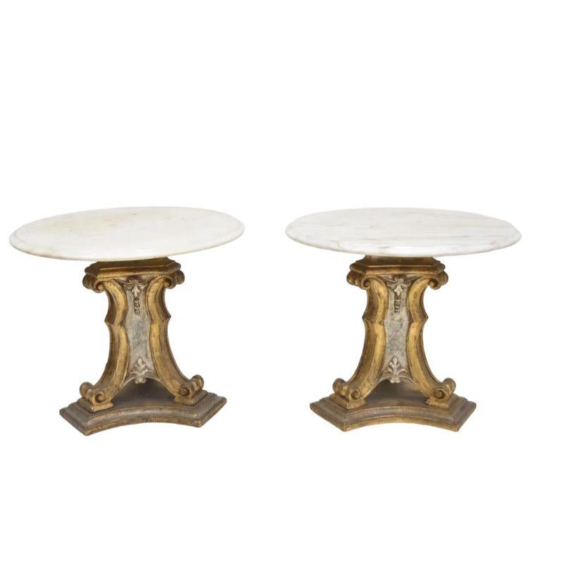 A vintage pair of Italian two tone gilt and silver tripod pedestal side tables with round marble tops. Each base has a carved, scroll form base with acanthus leaf and bead detail and a white marble top with beveled edge.
