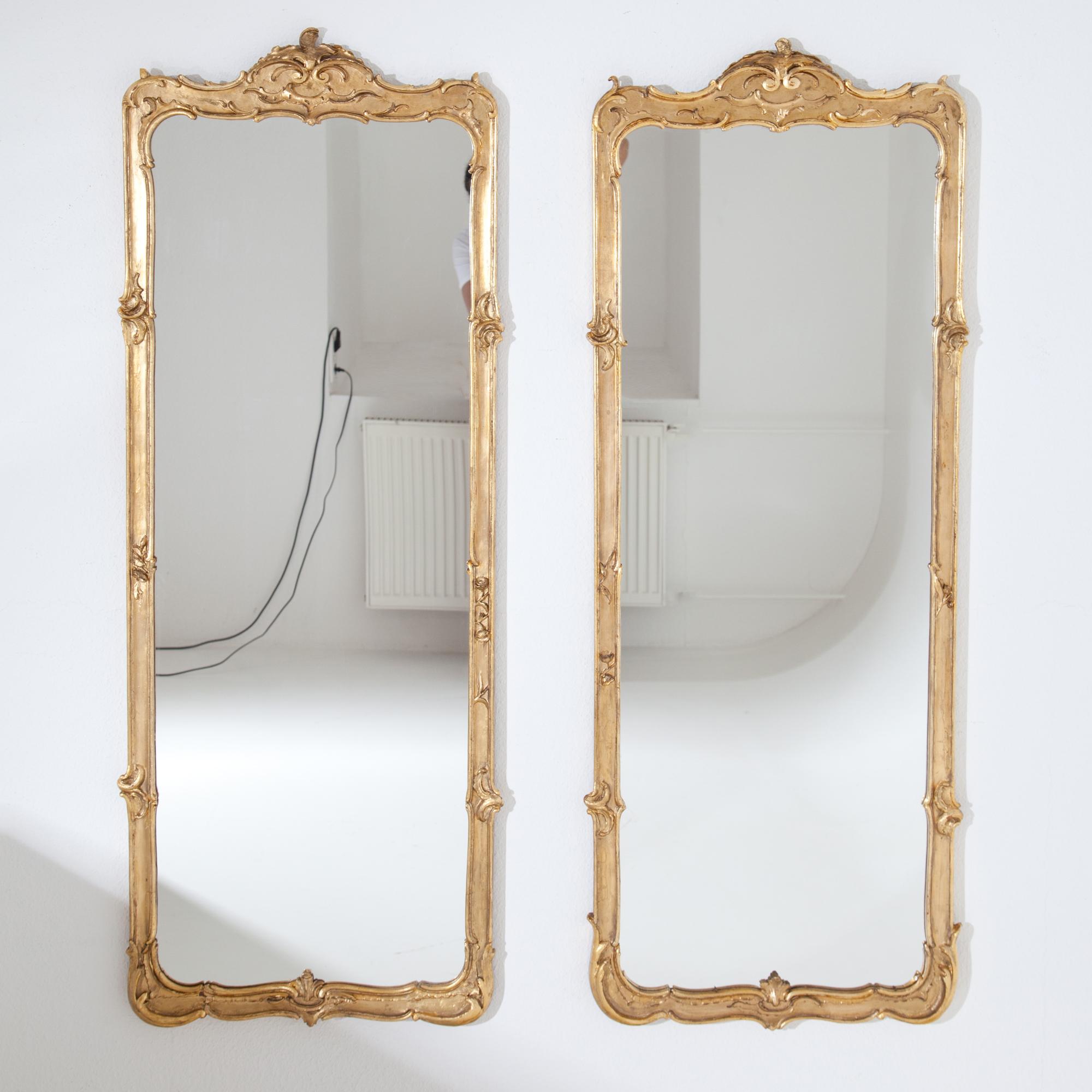 Pair of rectangular wall mirrors in golden patinated, slightly asymmetrical frames with rocaille and leaf decoration in rococo style. Gilding added. Probably former parts of a paravent converted into mirrors.