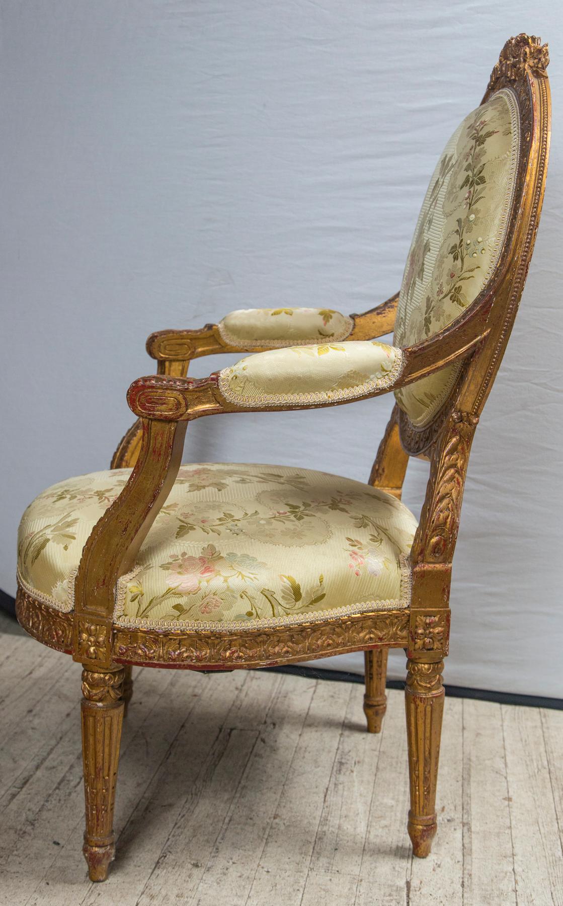 The round upholstered back topped with a hand carving of roses, other flowers and a ribbon. The entire frame carved with leaf decoration. Fluted tapering legs in the Louis XVI manner. Well detailed carving.
Wide spreading padded arms, wide and deep