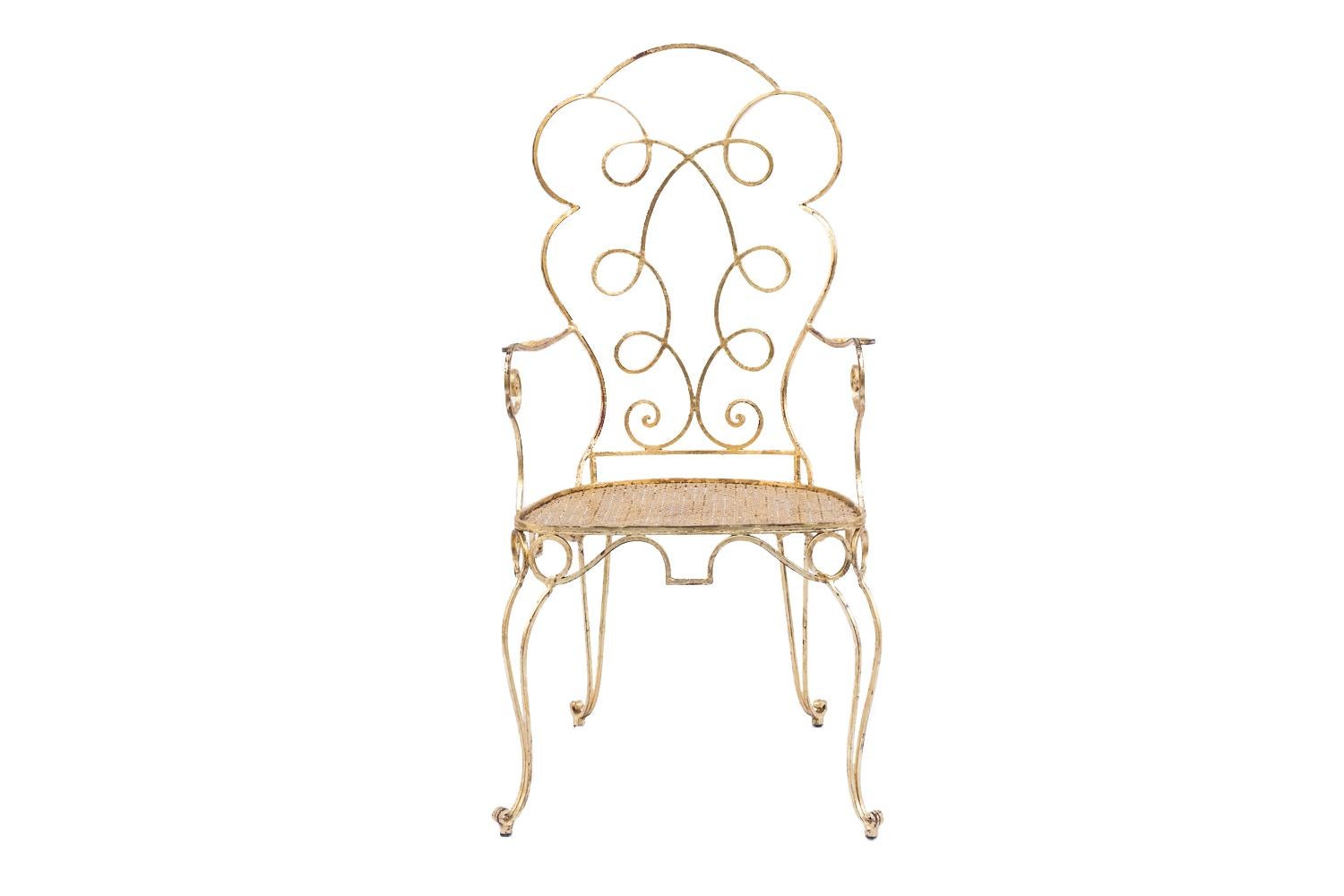 Pair of gilt wrought iron armchairs with curved shapes standing on four slightly curved legs finishing in scrolls. Tormented back with a motif of tracery. Scrolled armrests supports slightly beneath the leg line. Seat with an openwork decor