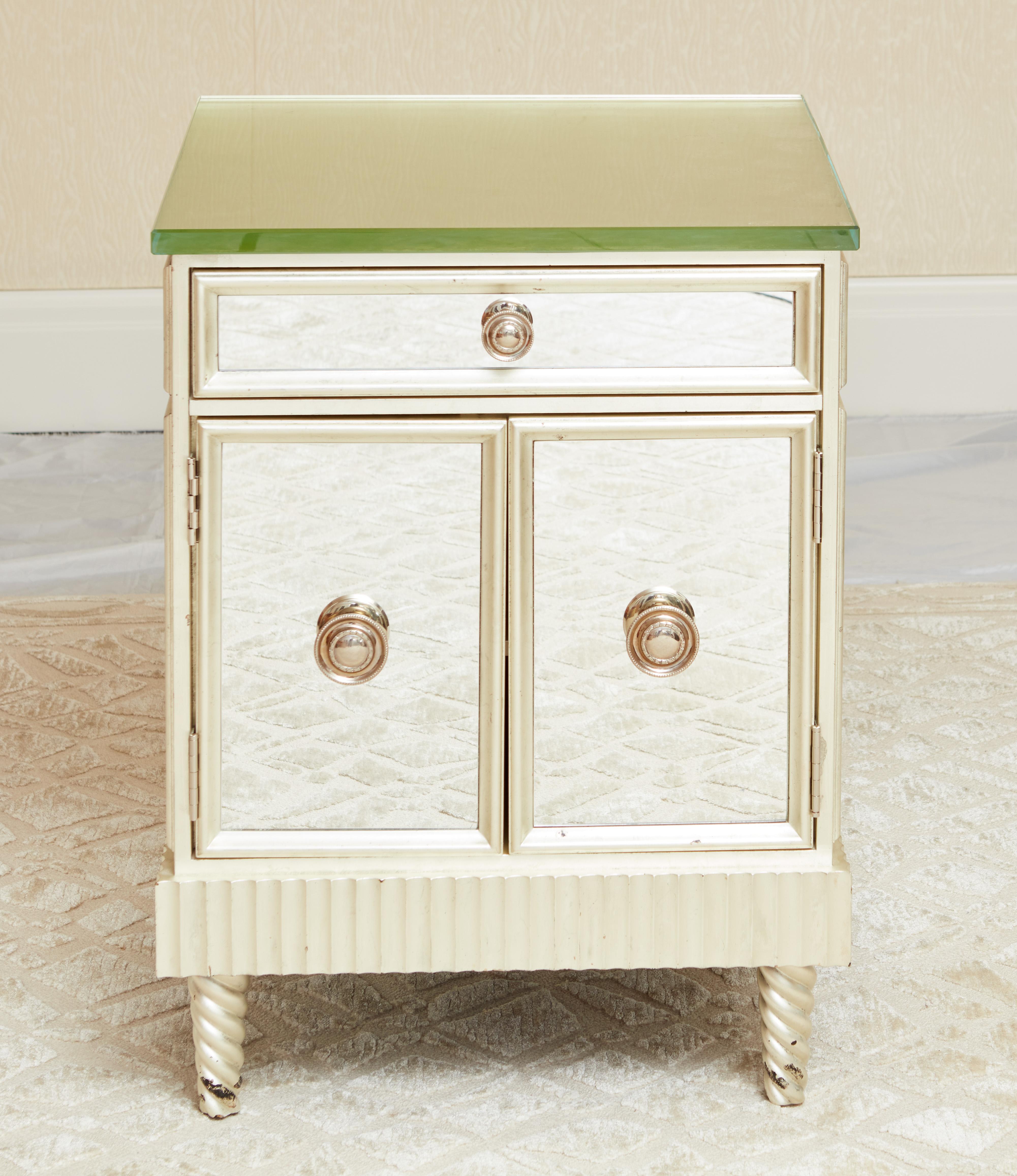 A beautifully crafted pair of custom designed white gold gilt and mirrored nightstands, the top having thick glass. The front with one drawer over a pair of doors all with nickel handles, supported by spiral carved feet.