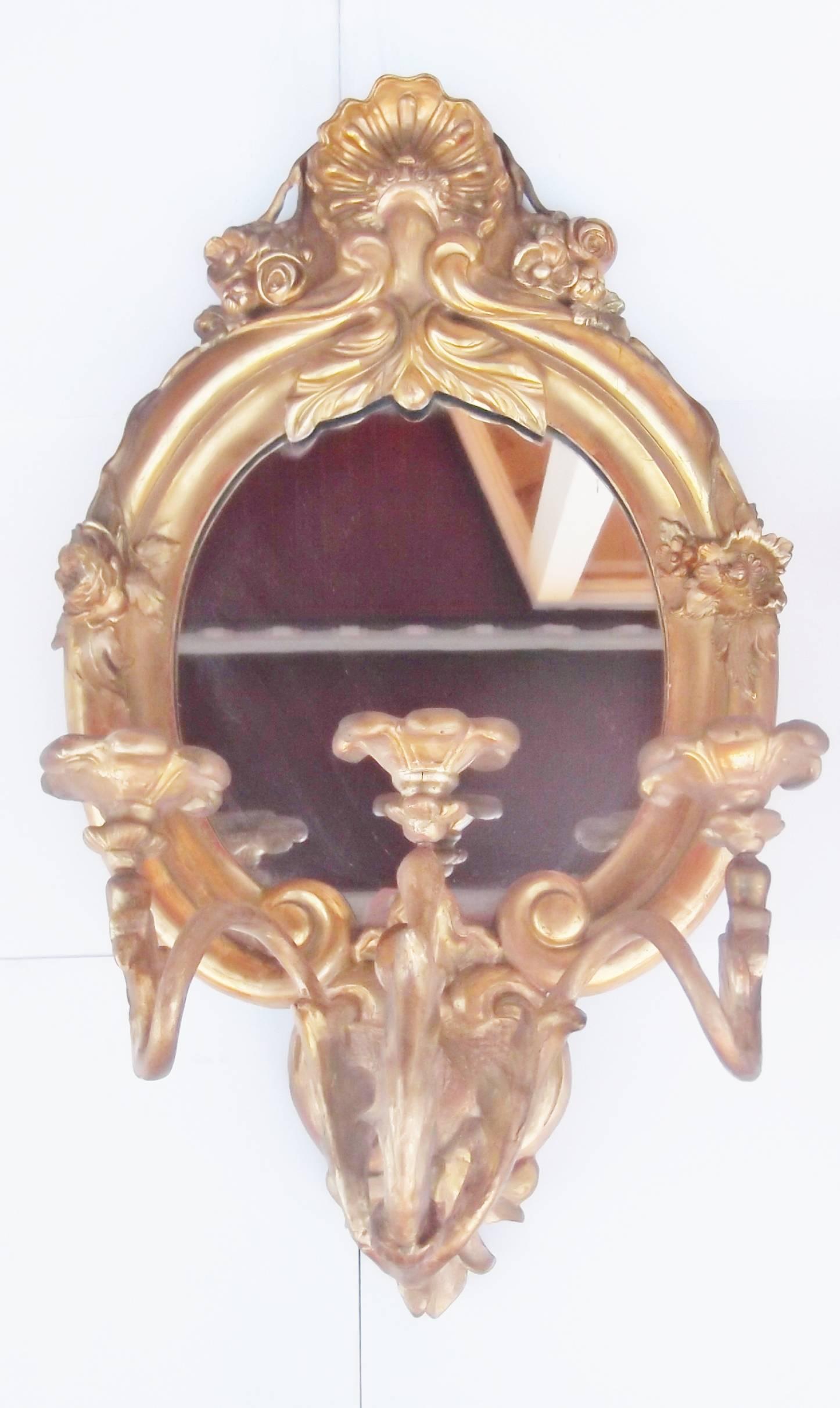 A pair of carved giltwood three-light mirrored girandoles with shell motif tops.
Graceful oval mirror backs with a triple-arm candelabra attached to the front. A hard to find original pair in well cared for condition. Definitely European, made in