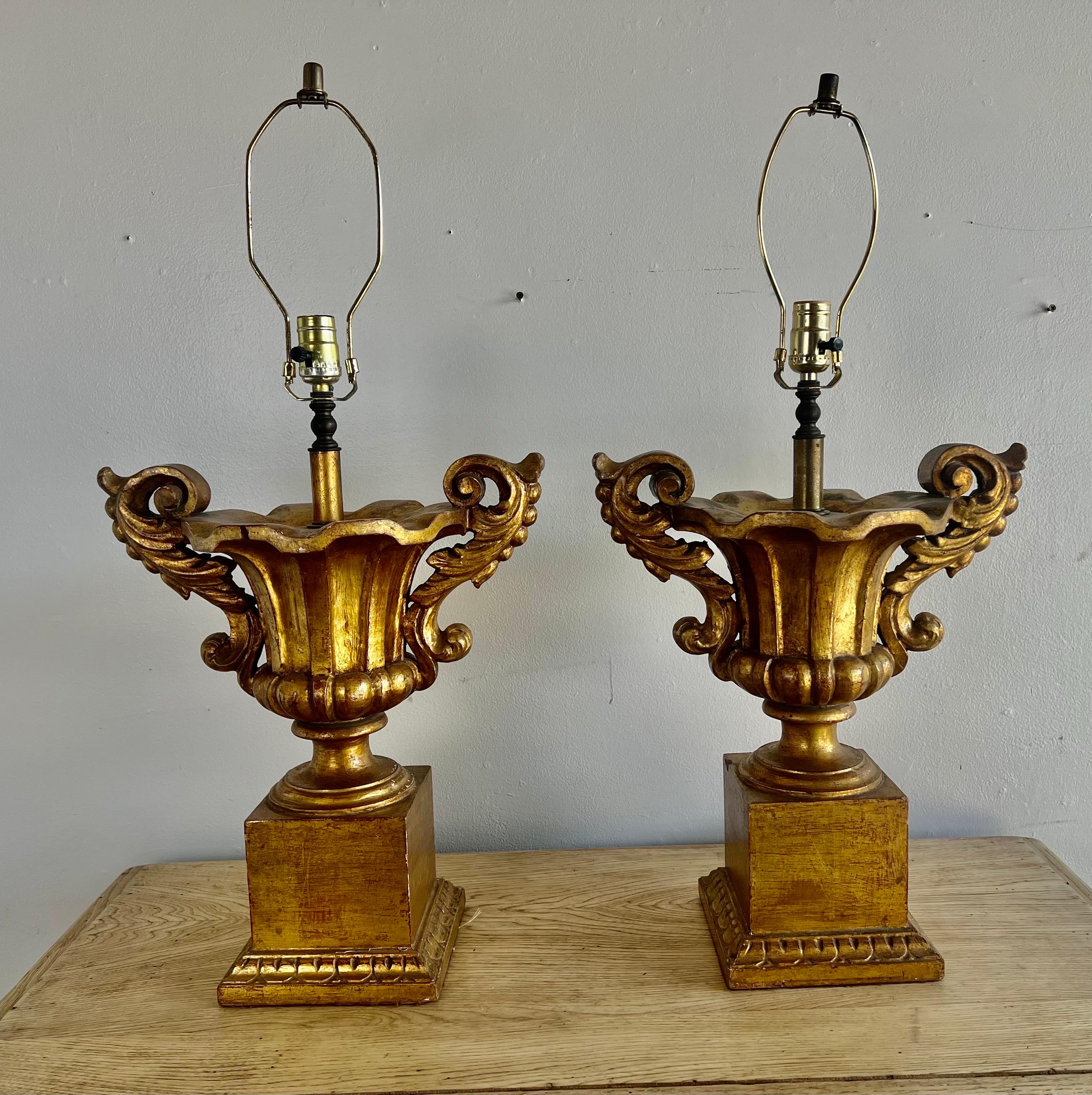Pair of Italian Neoclassical style giltwood urn lamps with carved acanthus leaves.  The urns sit on plinth bases.  The lamps are both in working condition.