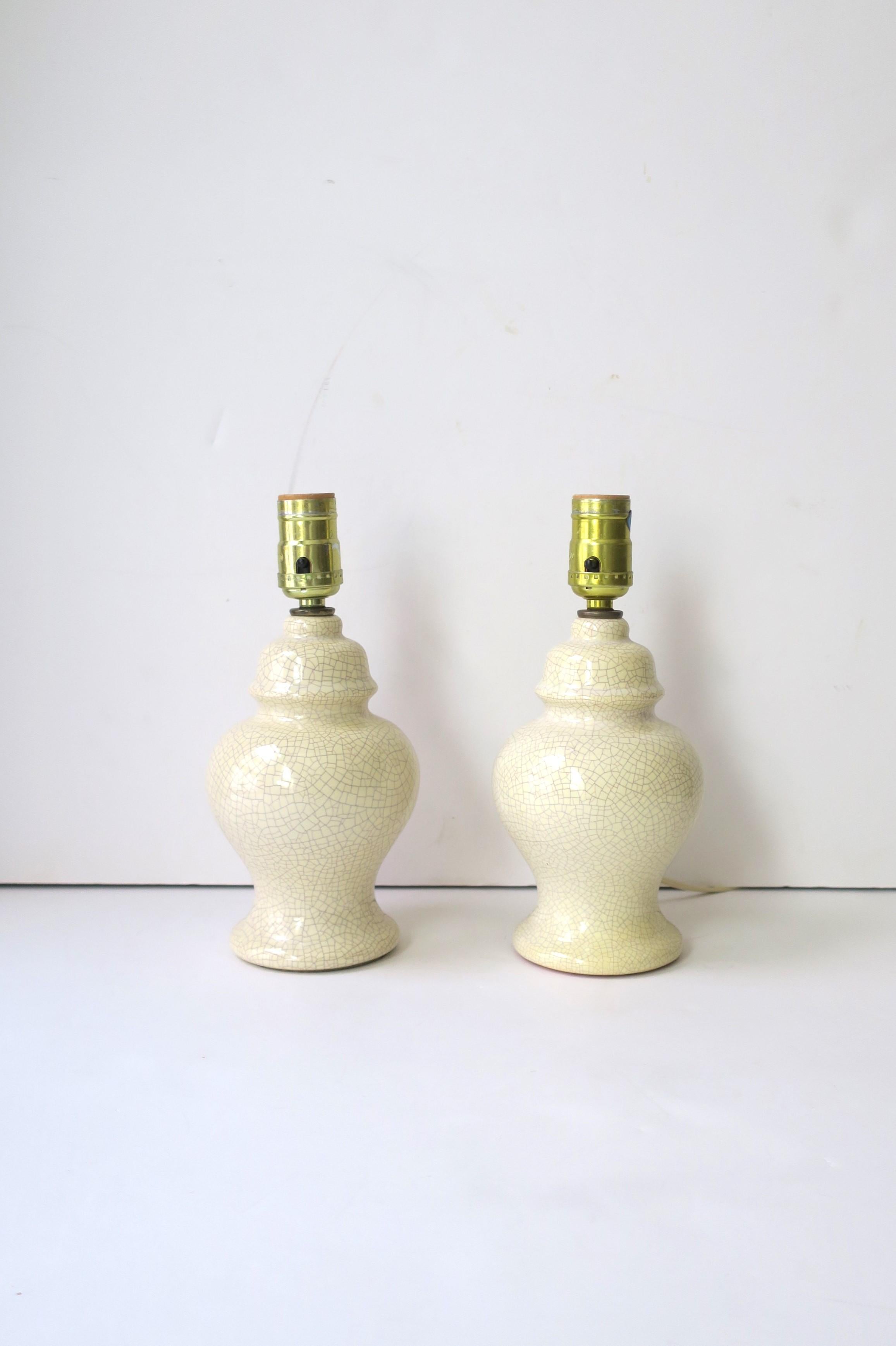 A pair of ceramic ginger jar table lamps, in the Asian Chinese style, circa mid to late-20th century, 1960s, 1970s. Ceramic hue is off-white/beige with a dark crackle. Cord is a nice length measuring. 85.5