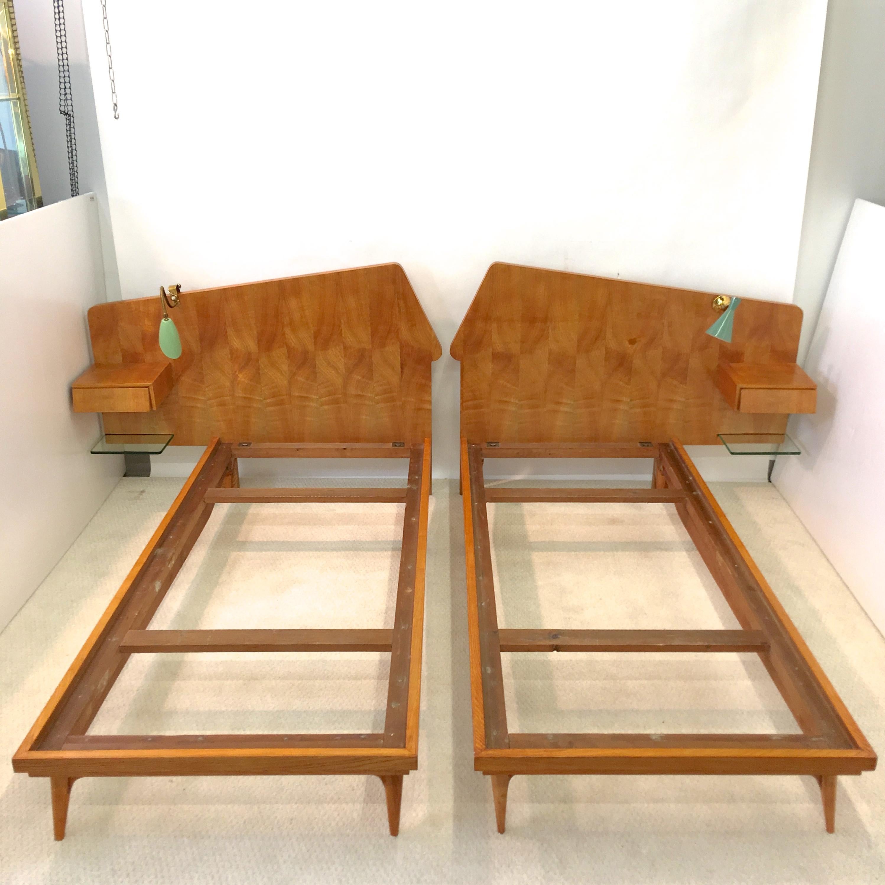 1950s Italian pair of twin beds in light color finished birch wood with highly figural book matched birch veneer asymmetric headboards mounted with floating nightstands with a single drawer having stylish angled drawer face and floating glass shelf