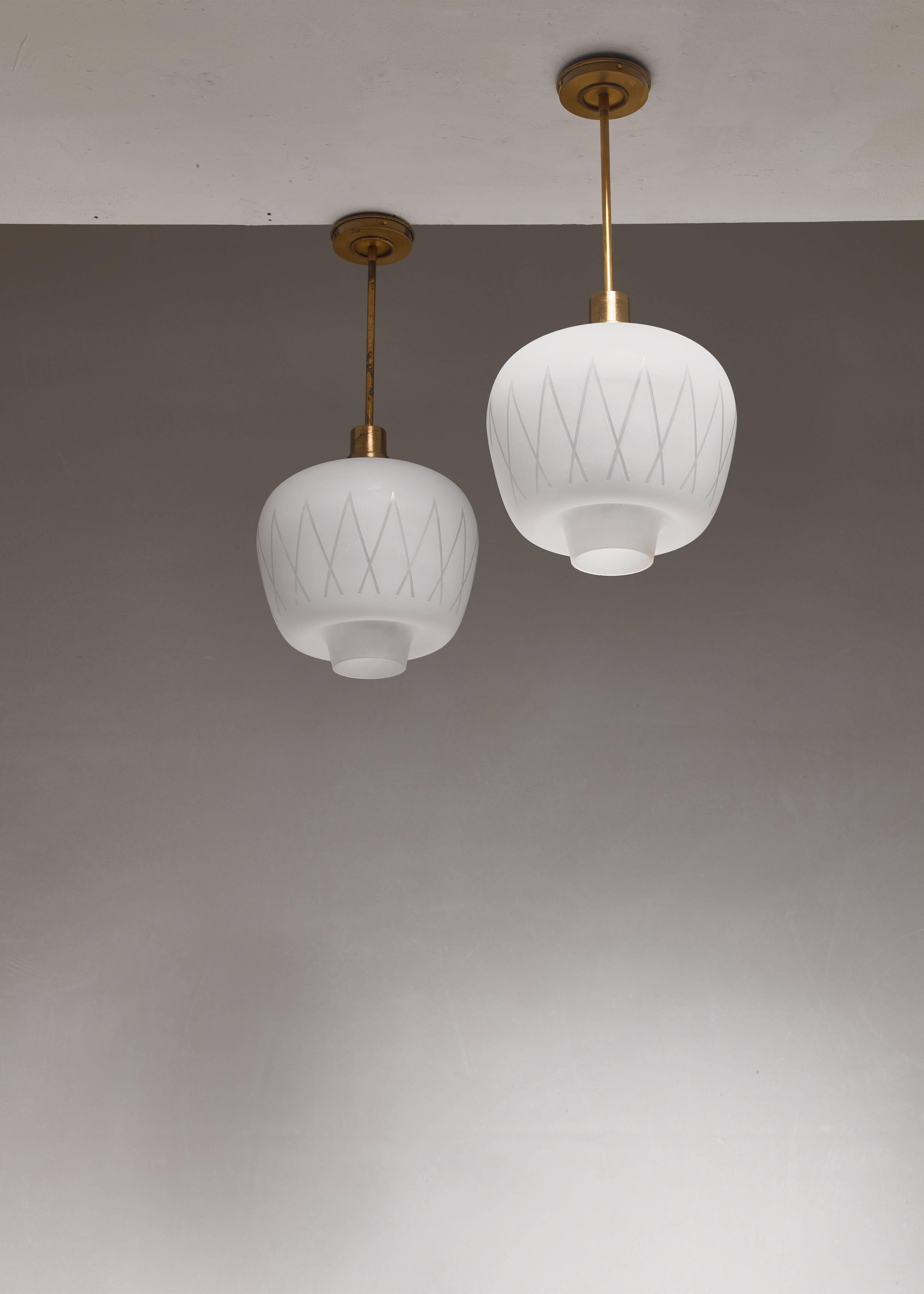 A pair of Swedish midcentury pendant lamps, made of a frosted glass shade with a geometric pattern, hanging from a brass mount. The design is reminiscent of the lamps by Hans Bergström for Lyktan.

The height of the shades is 25 cm. The total drop