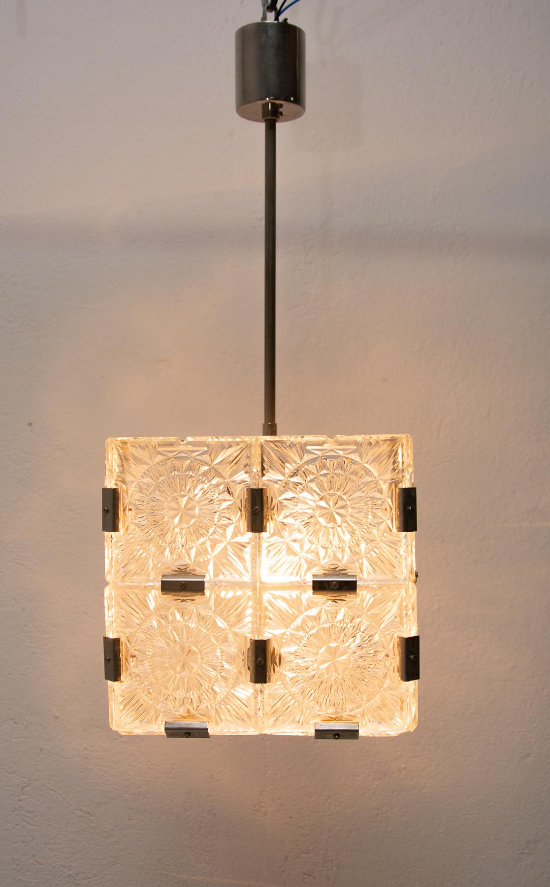 Glass and chromed cube pendant lamps, 1970s, Czechoslovakia. It was produced by Kamenický Šenov. It is made of glass and metal. It´s composed of thick textured patterned square cut fetal pieces with chrome fittings.
It was completely professionally